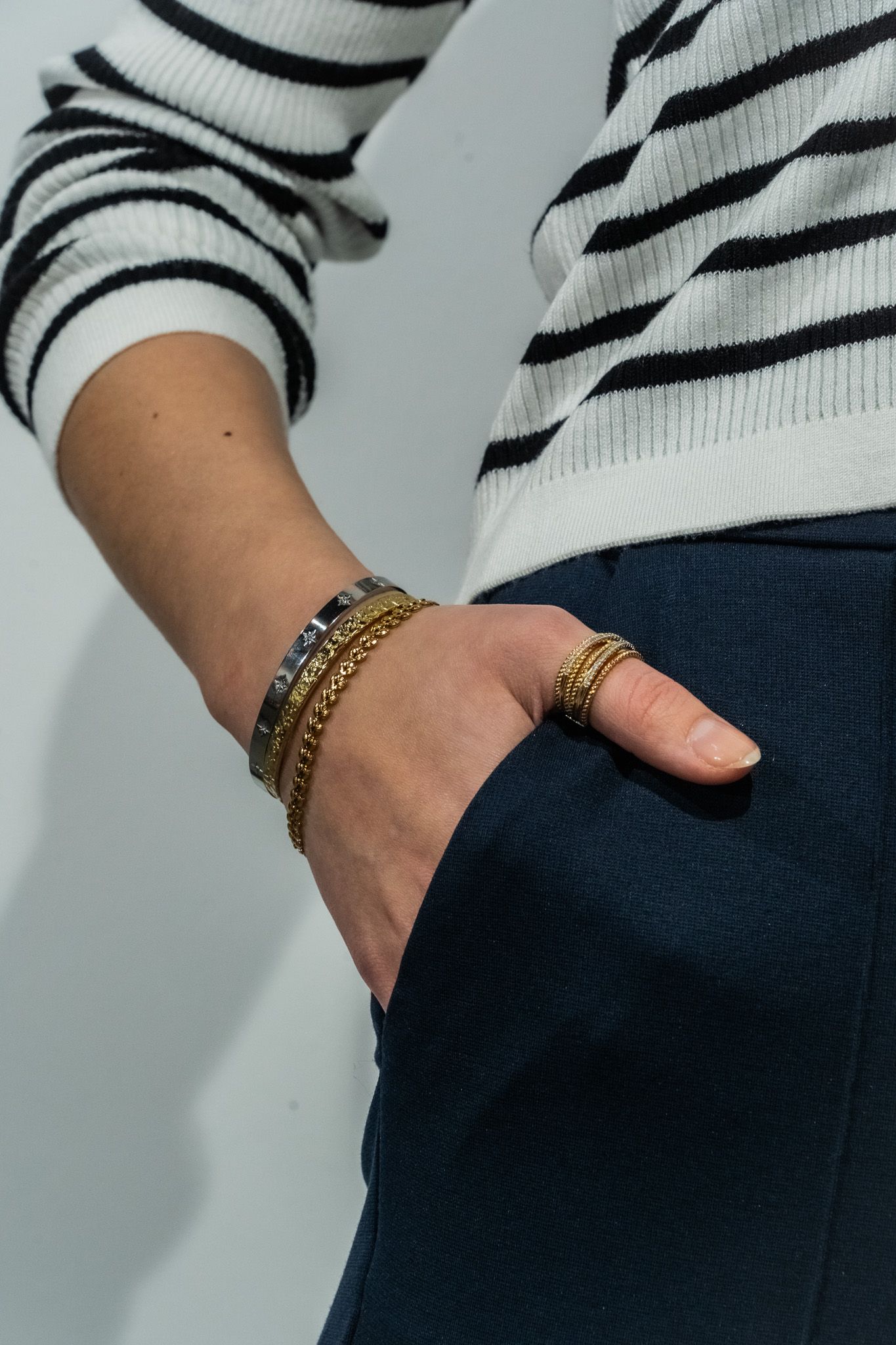 Person wearing a striped sweater showing gold bracelets and rings against dark pants.