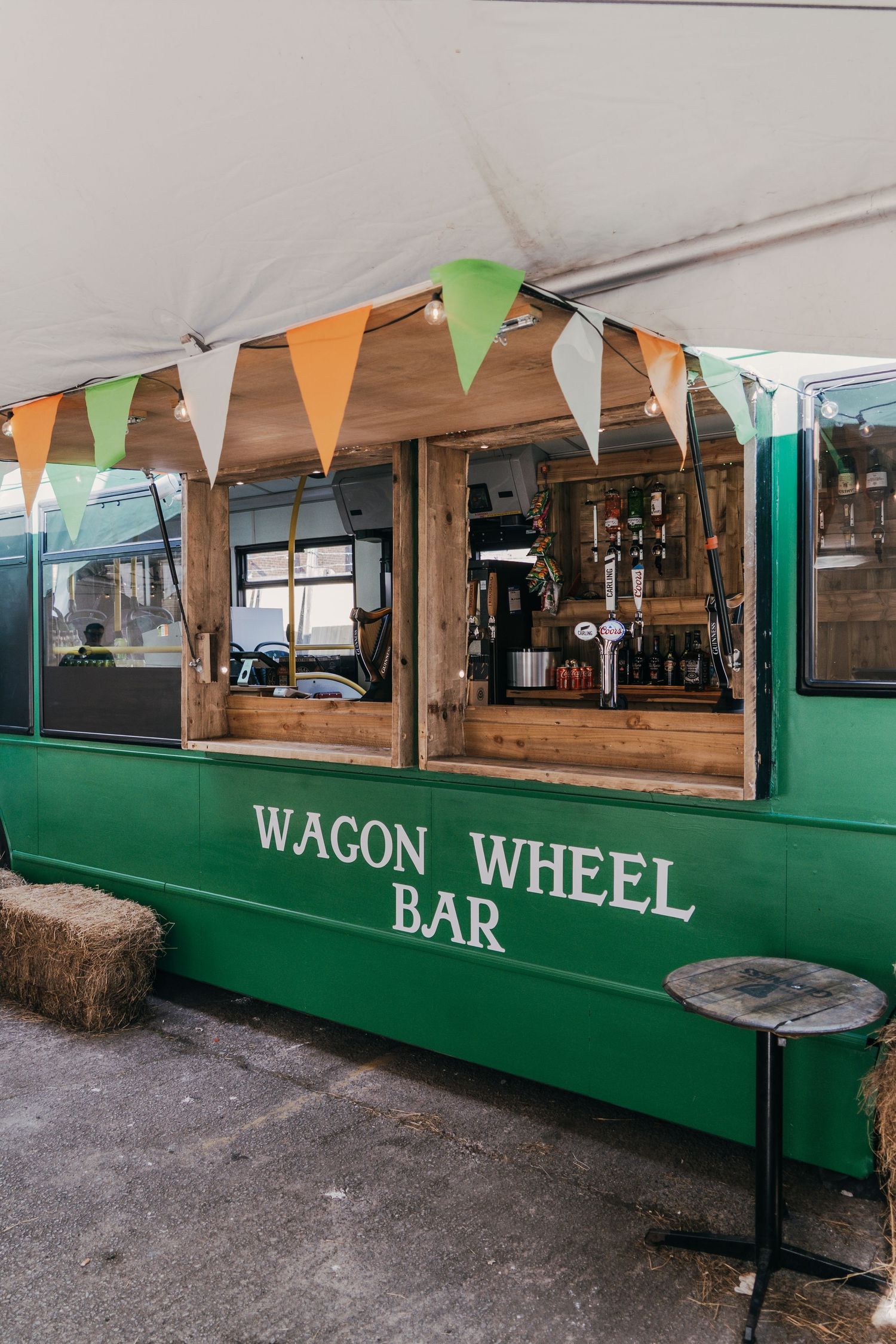 Green Wagon Wheel Bar mobile stand with festive orange and green bunting flags decorating the wooden counter area.