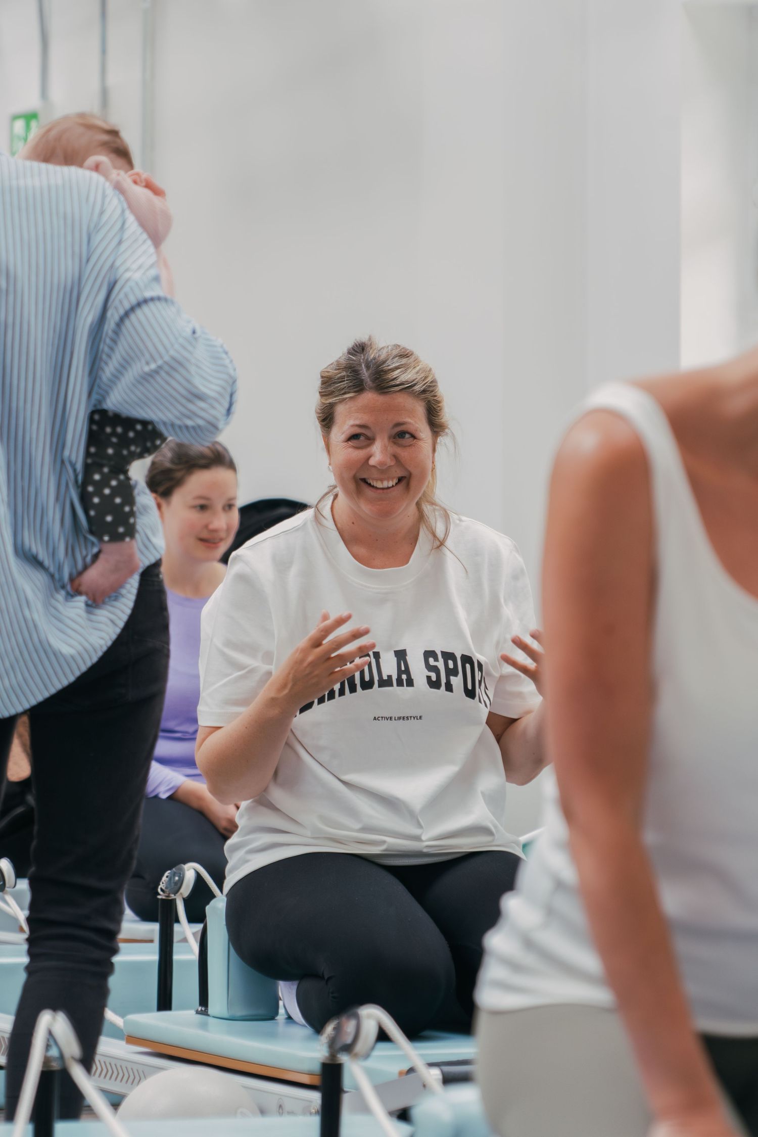 Person wearing a white t-shirt laughs joyfully during what appears to be a group exercise or wellness session.