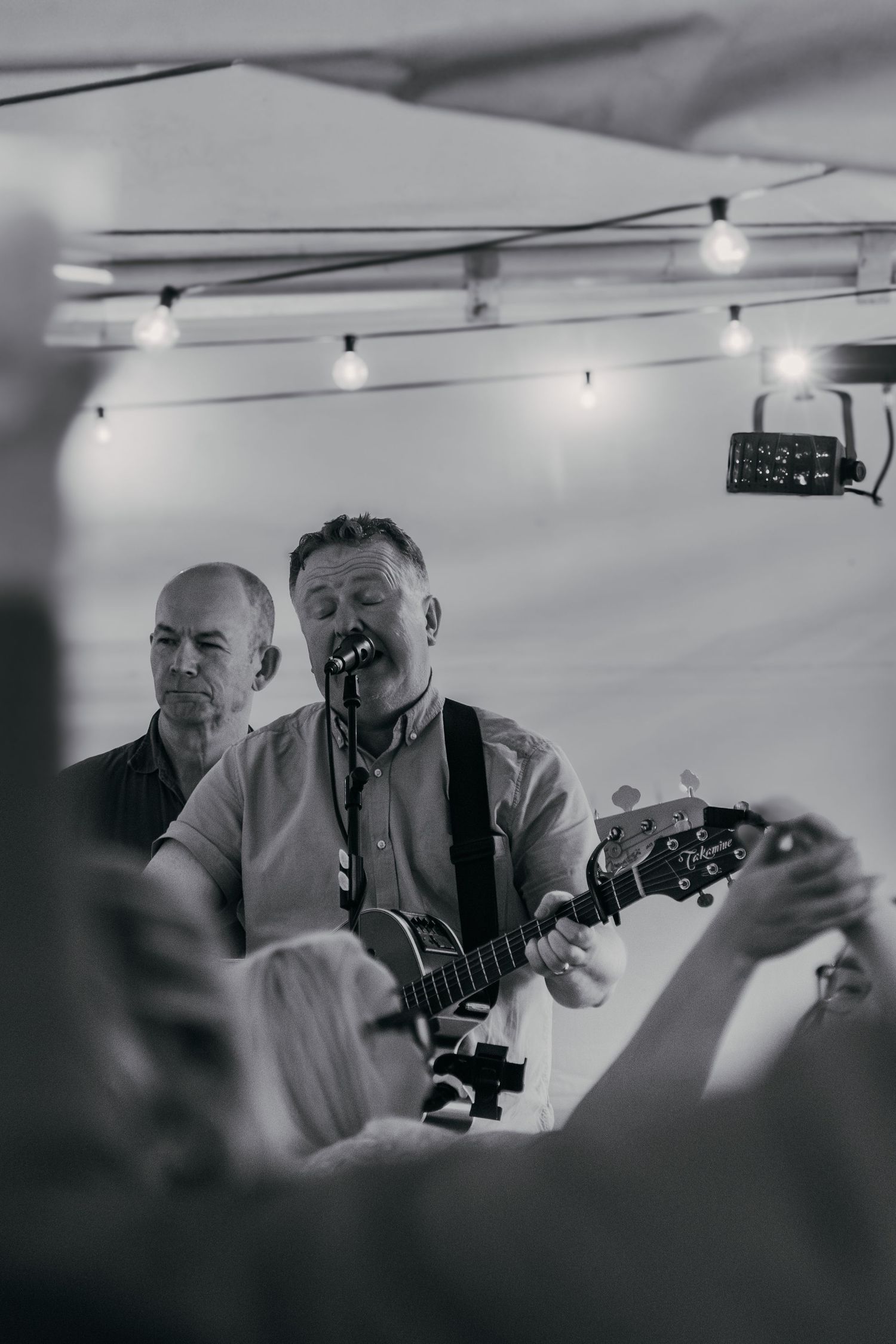 Musicians performing on stage with string instruments under hanging lights in a black and white photograph.
