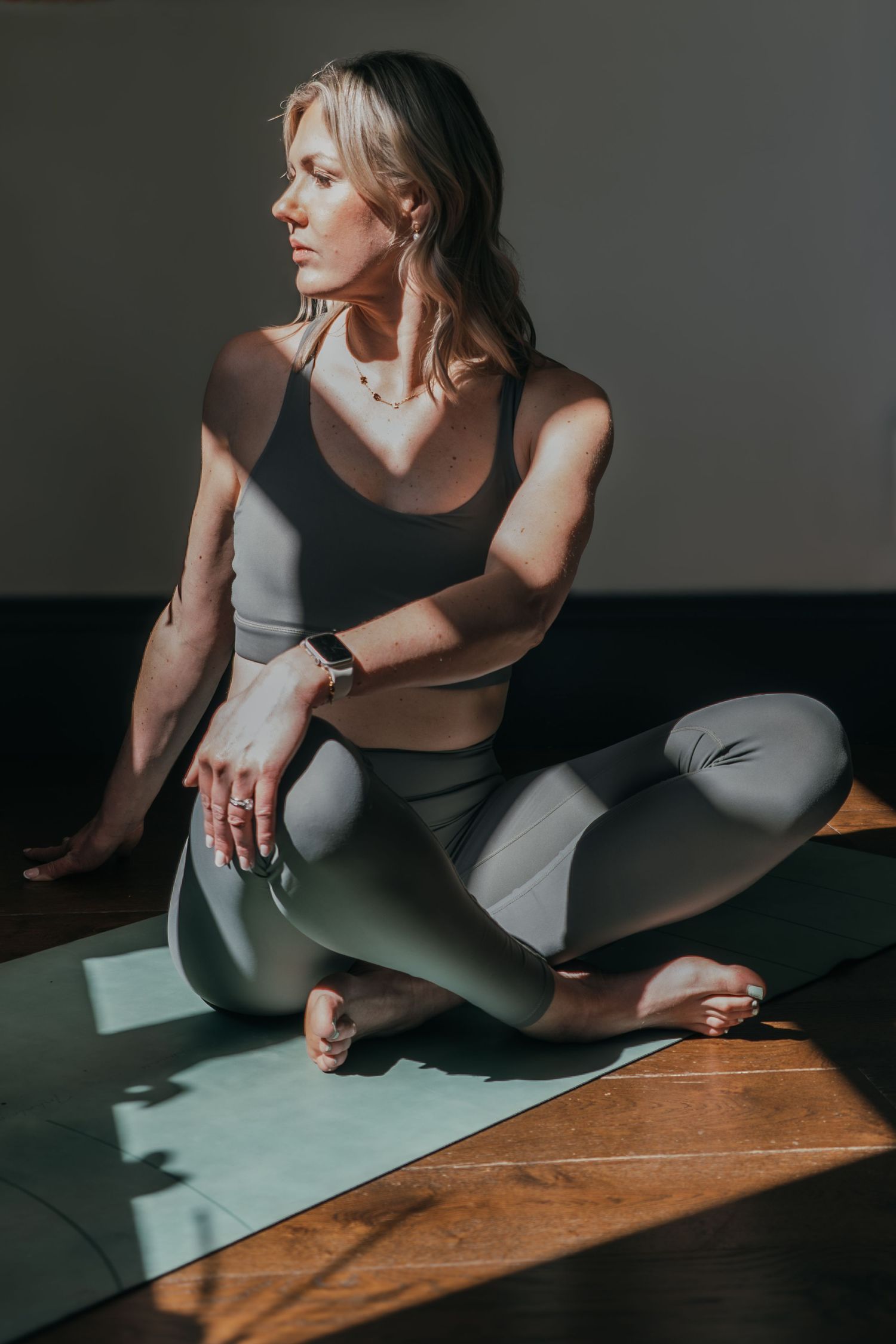 Athletic person in workout attire practicing yoga on a mat in dramatic lighting with striking shadows.