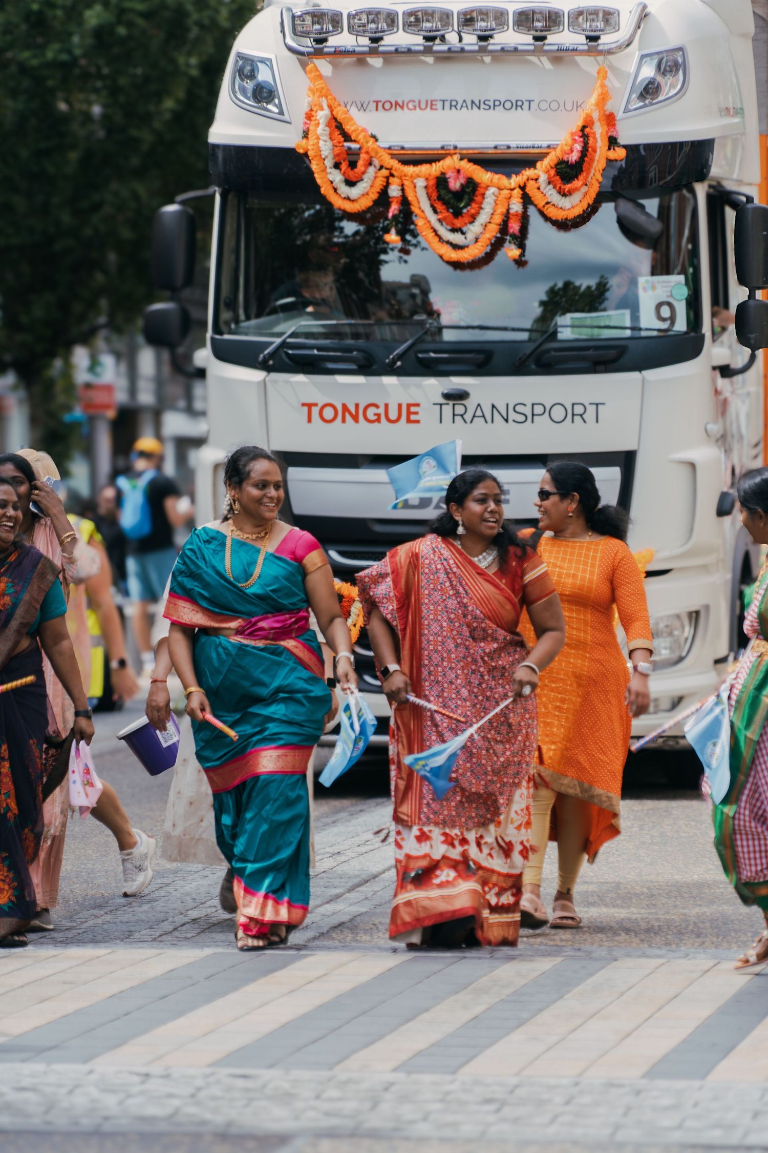 Group of women in colorful saris celebrating near decorated transport trucks during an Indian cultural festival.