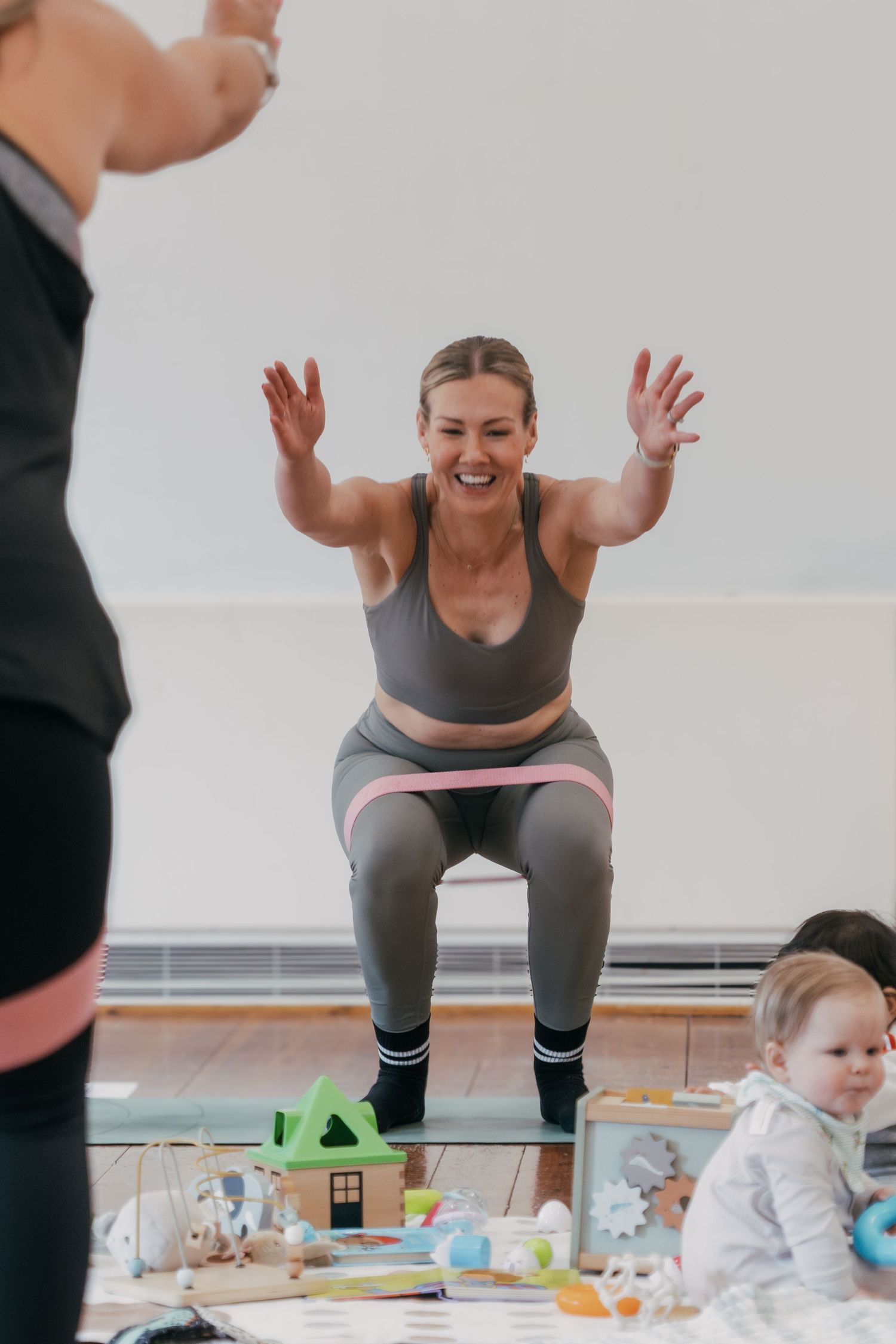 A person in workout clothes doing squats in a room with toys and children's items scattered on the floor.