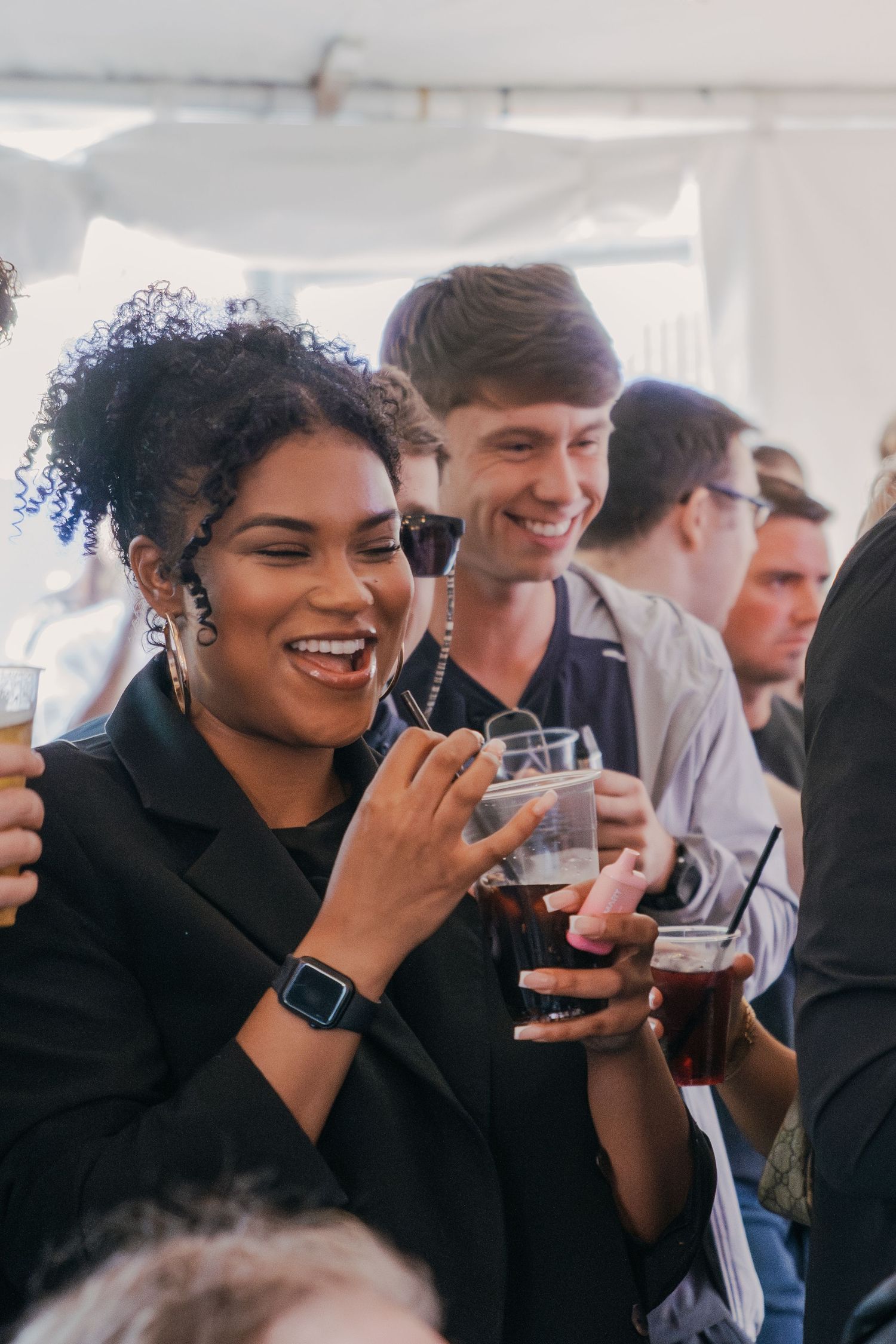 A lively celebration scene under a white tent with people enjoying drinks and laughter together.