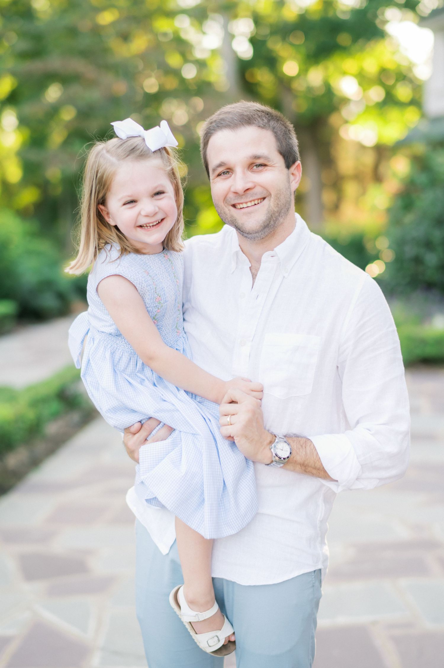 Parent and child in coordinated blue and white outfits pose on stone pathway in garden setting.