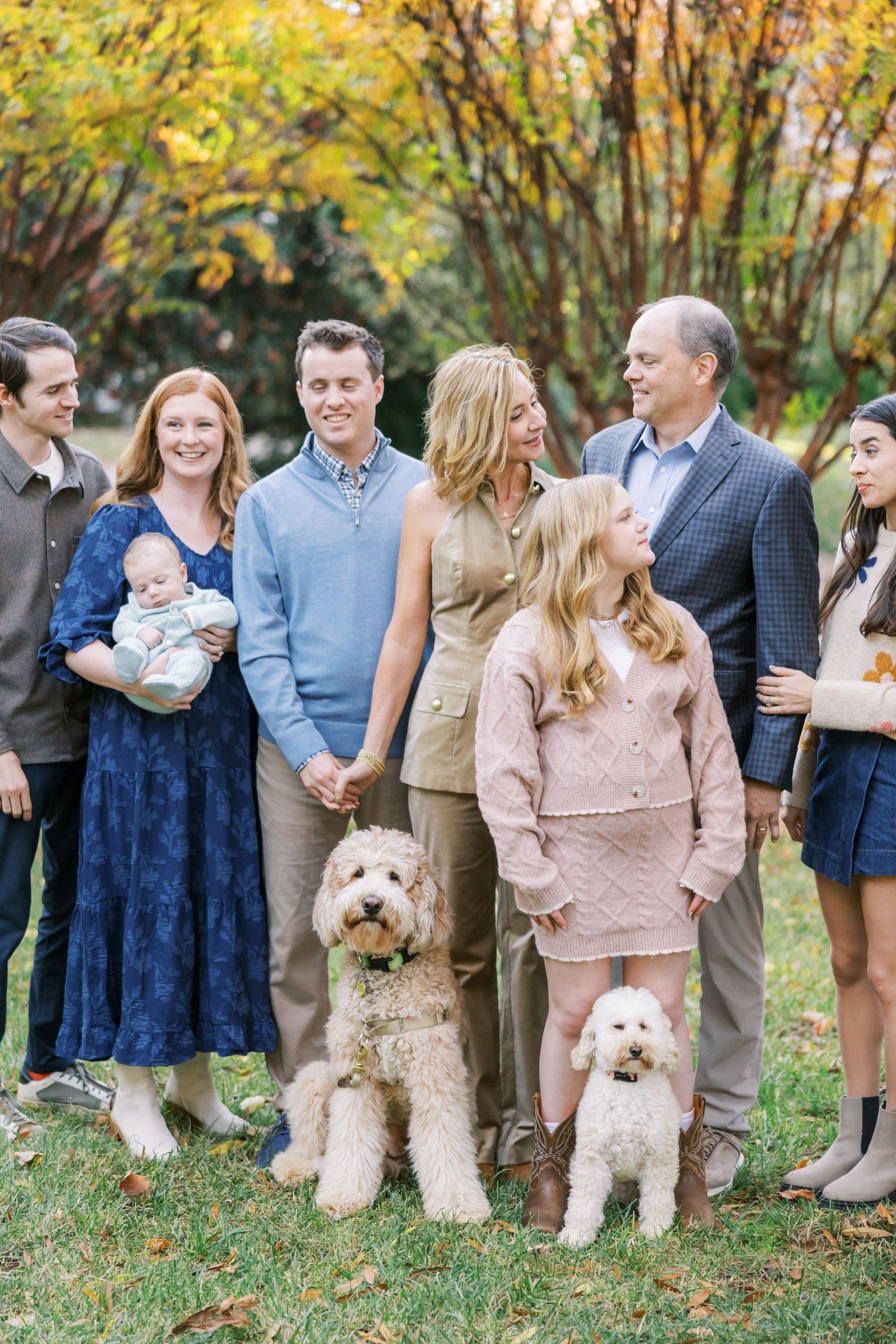 Extended family portrait outdoors with two fluffy dogs on a fall day with autumn trees.