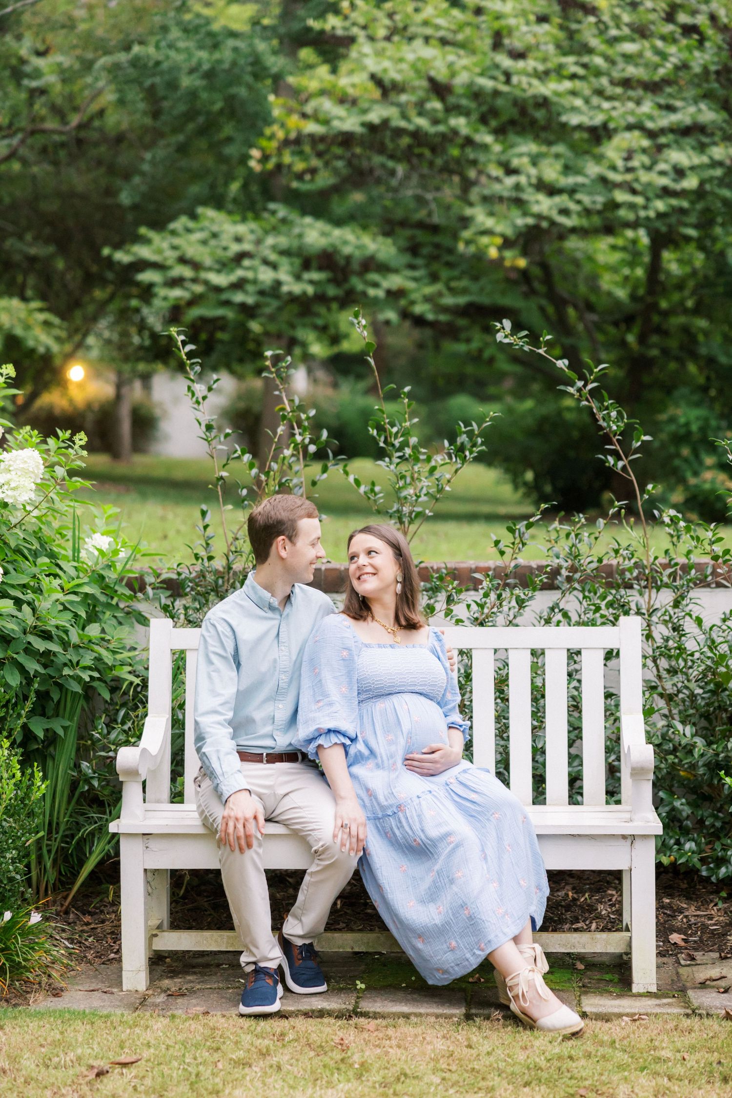 Romantic moment shared on white garden bench surrounded by lush summer greenery.