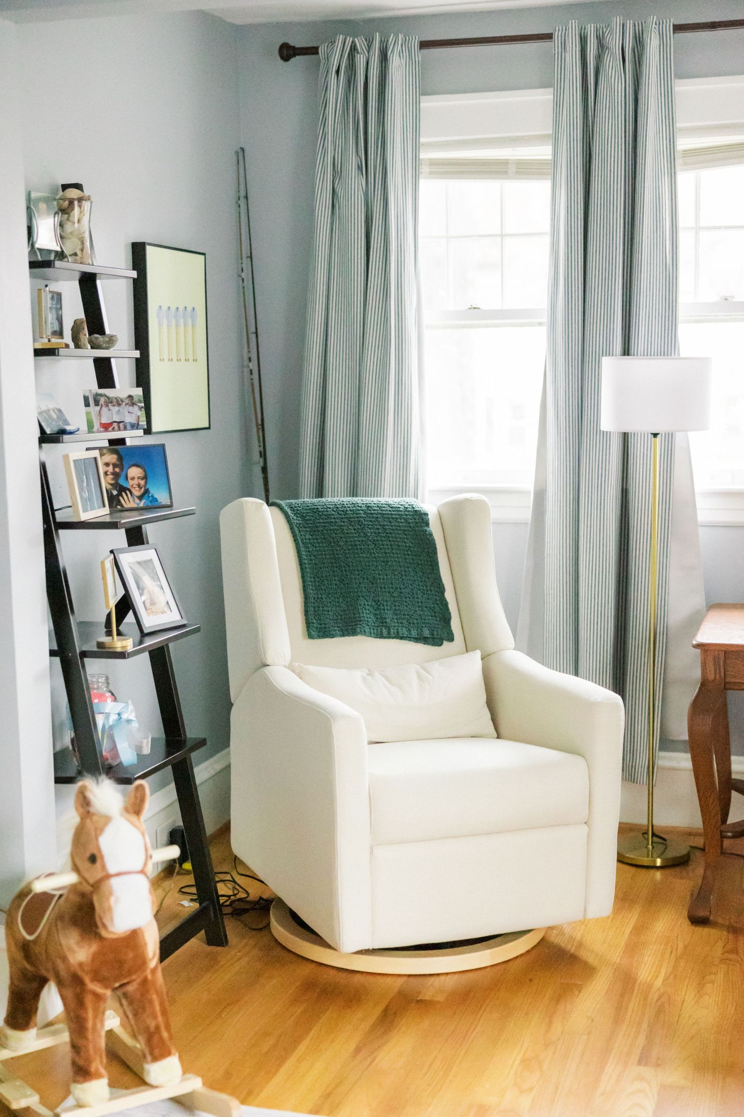 Modern nursery corner with white glider chair, ladder shelf, and plush giraffe toy.