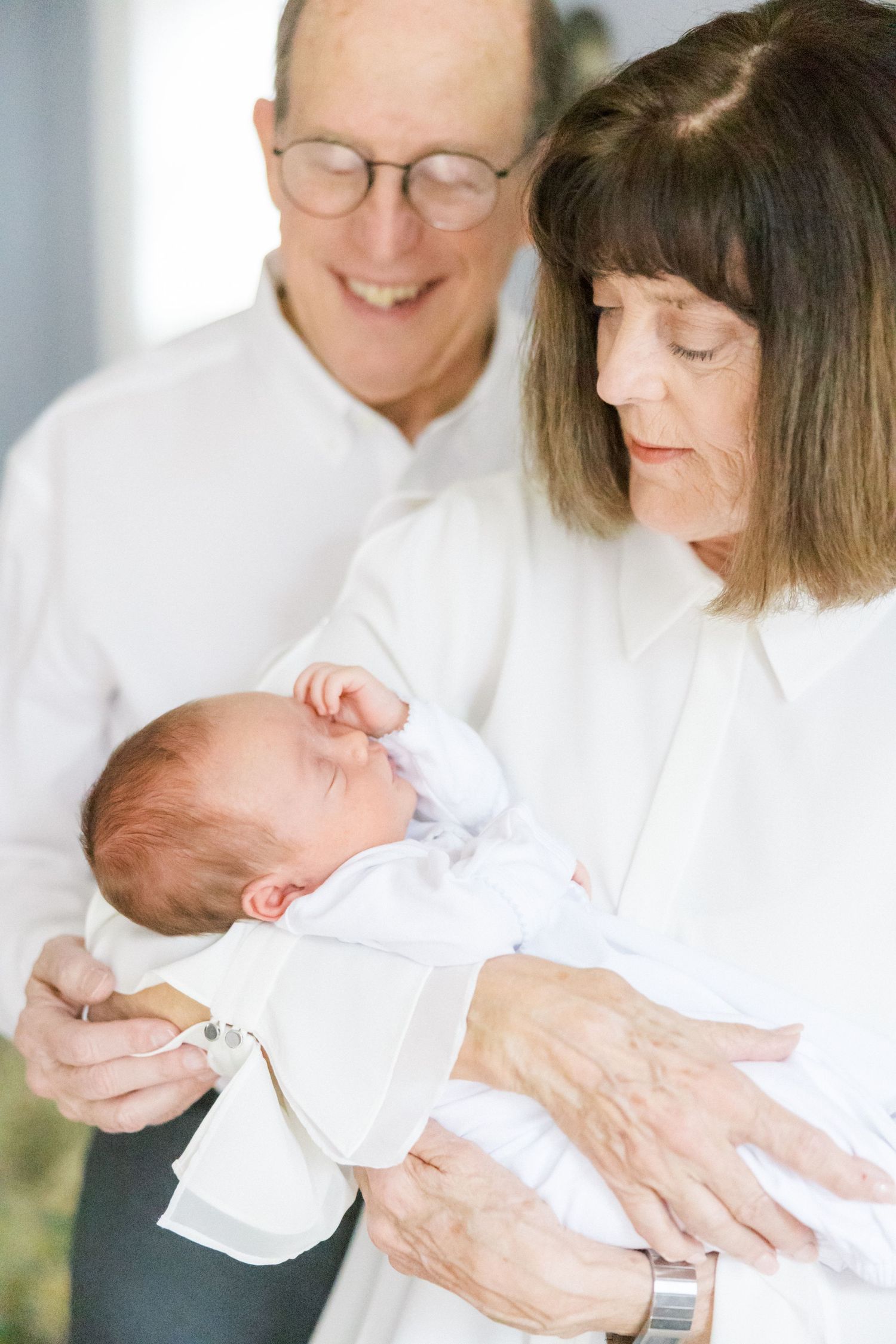 A couple shares a tender moment with their newborn baby, all wearing white.