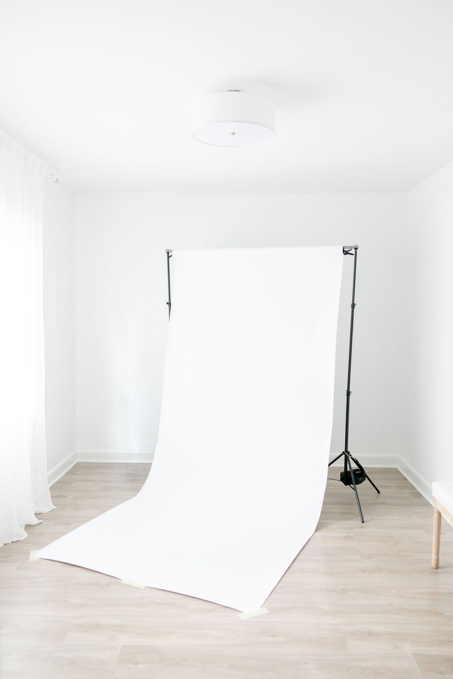 Professional photography studio setup with white seamless backdrop on light wooden floor against white walls.
