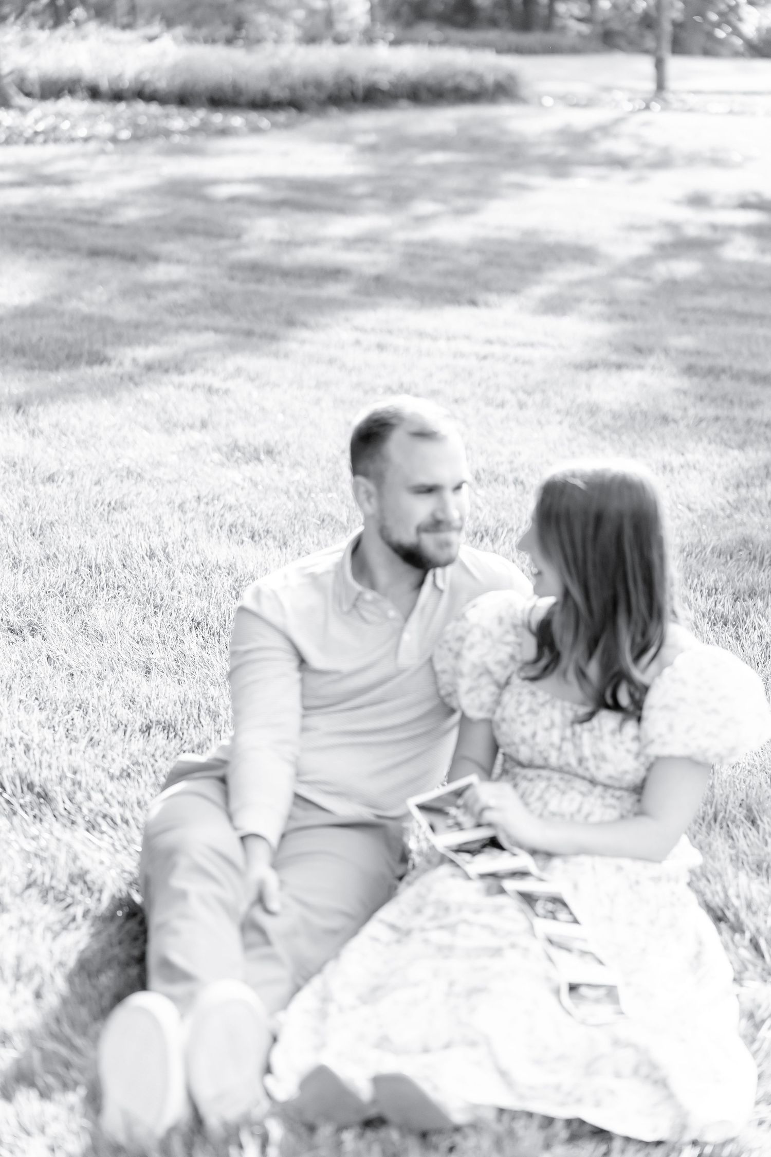 A couple sits together on grass having an intimate conversation in black and white photography.