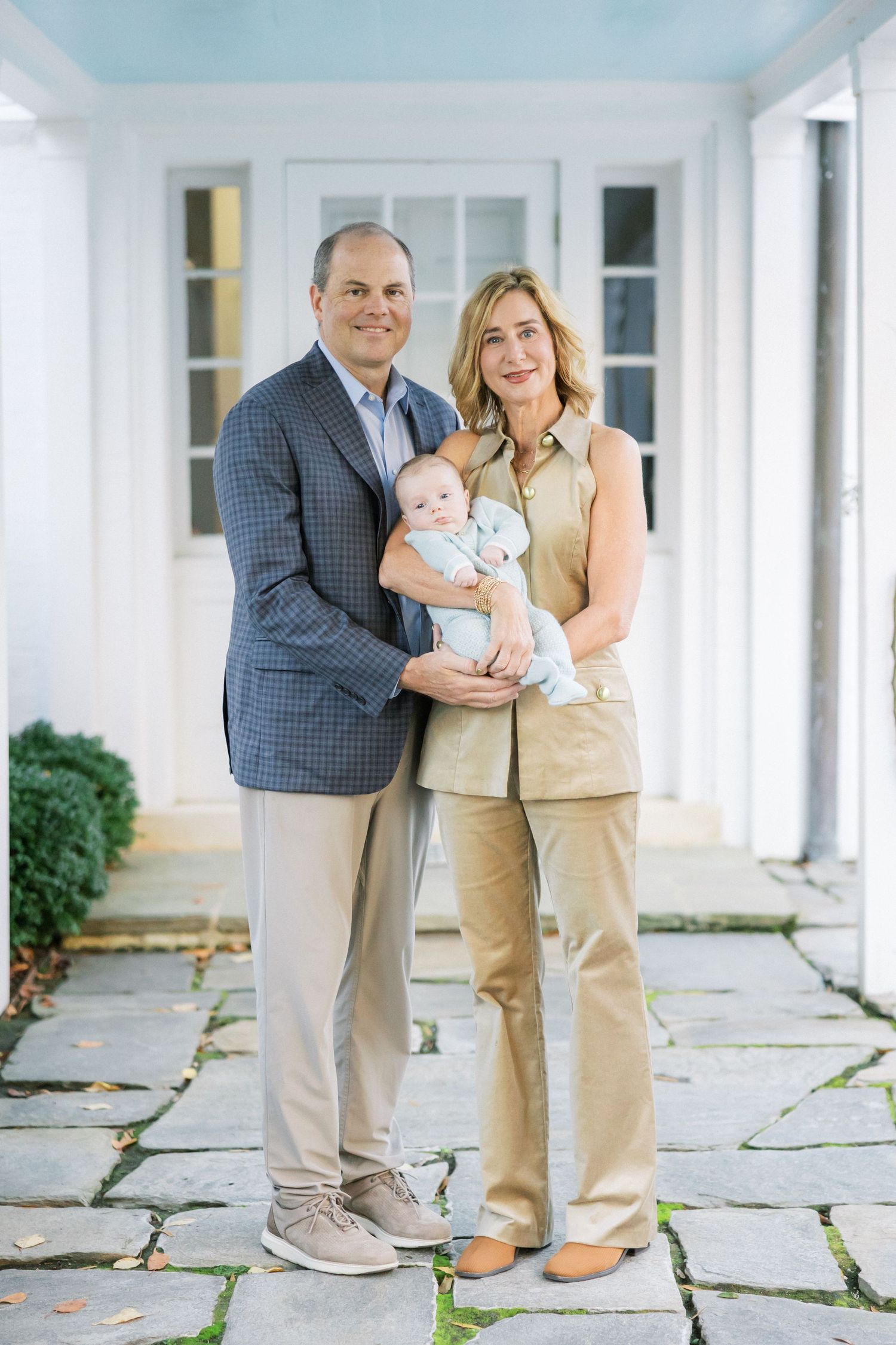 Couple with baby on white porch with blue ceiling and stone pavers.