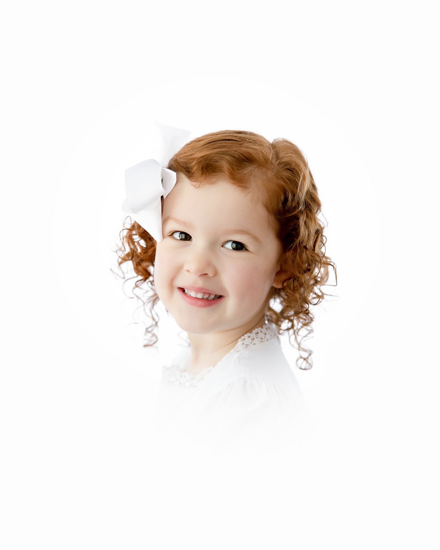 Cheerful young child with curly auburn hair wearing white against a white background.