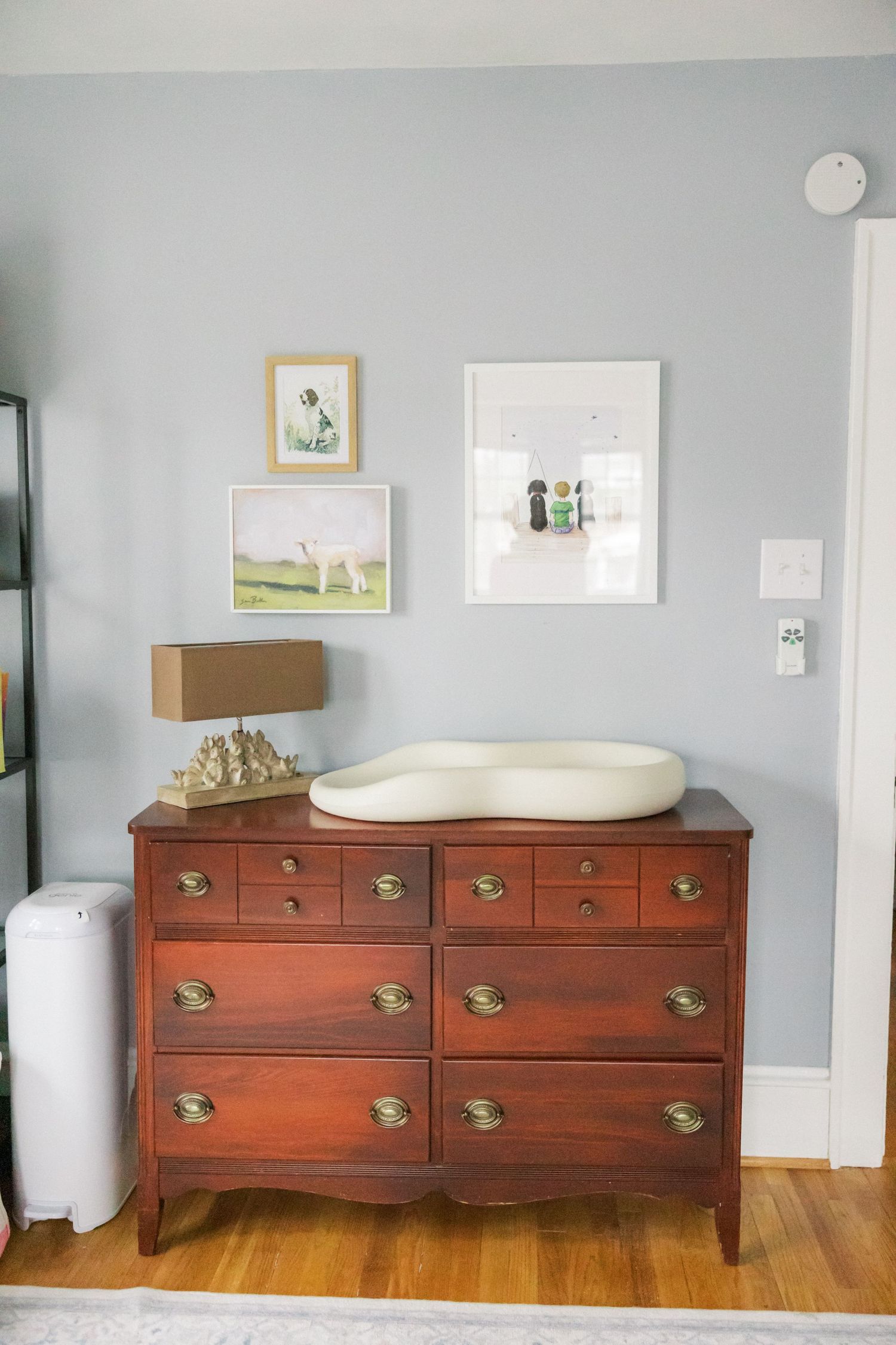 A vintage wooden dresser with brass handles styled with a lamp and changing pad in a nursery.