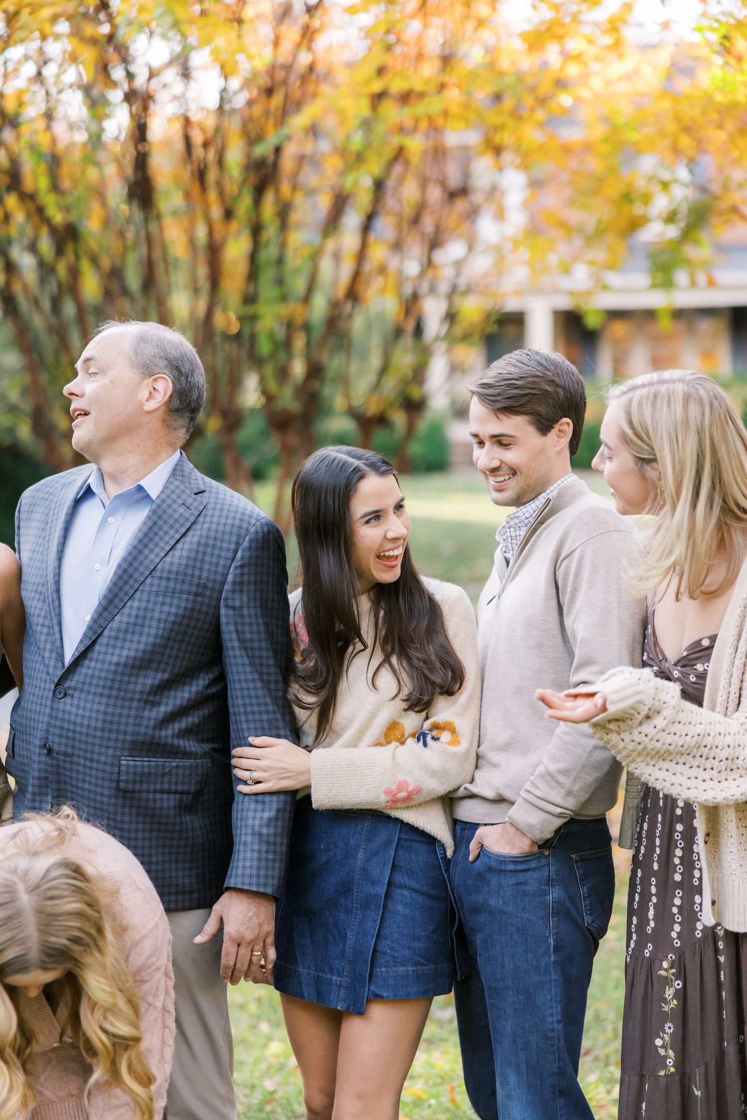 A small group of people share laughter together on a crisp fall day under trees with golden leaves.