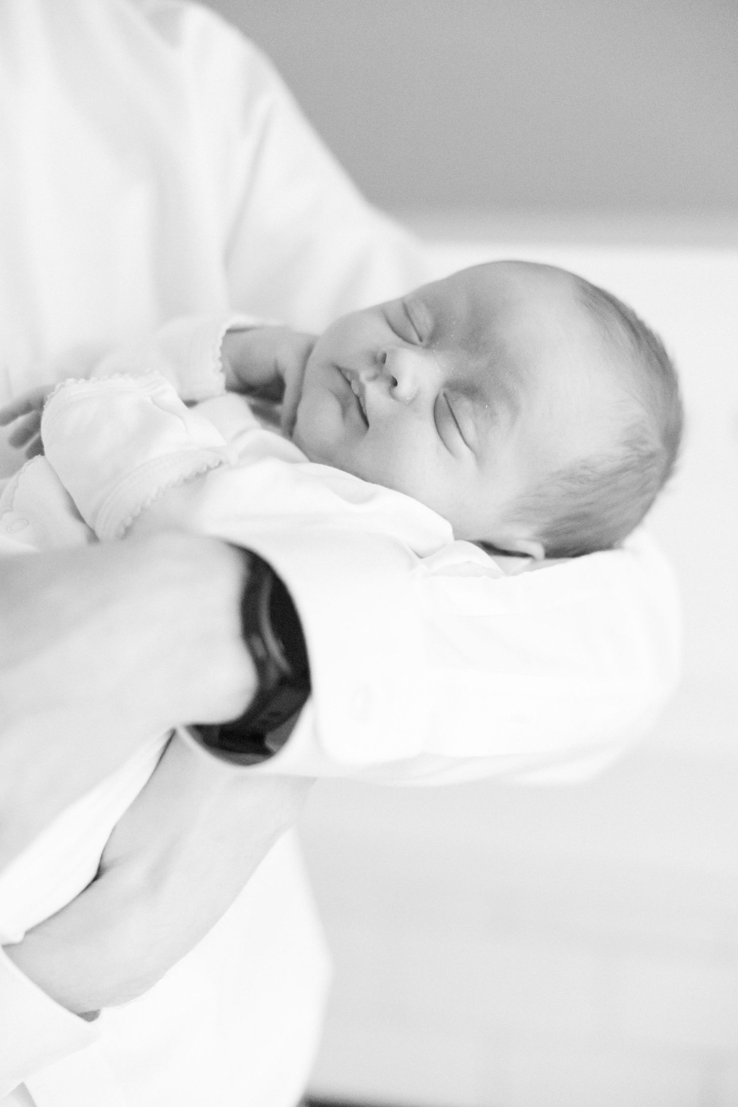 Peaceful sleeping newborn baby swaddled in white blanket against light background.