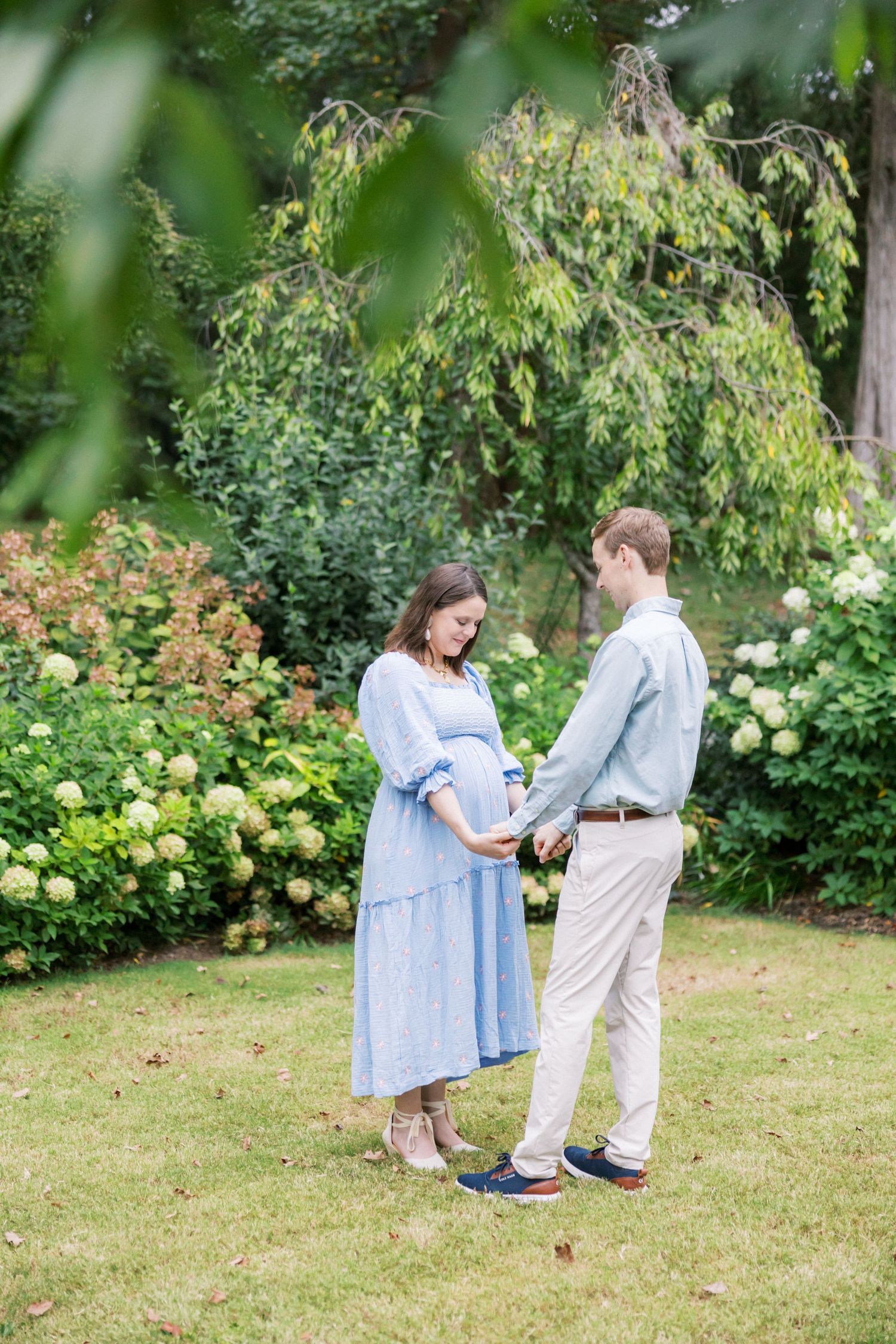 A couple stands together on a garden lawn surrounded by yellow roses and lush greenery.