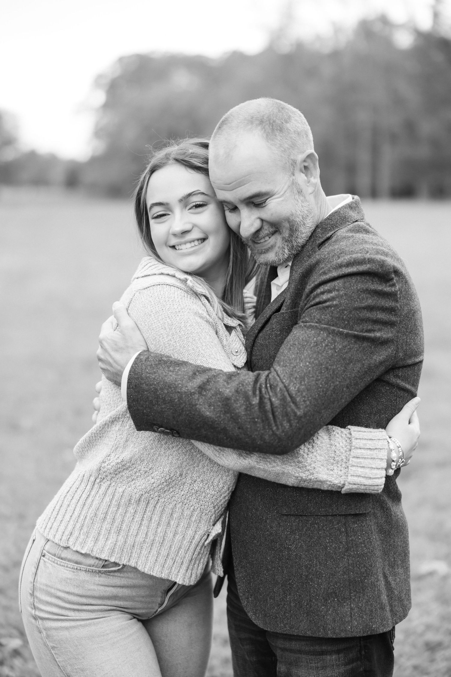 A black and white portrait captures an intimate embrace between two people in sweaters outdoors.