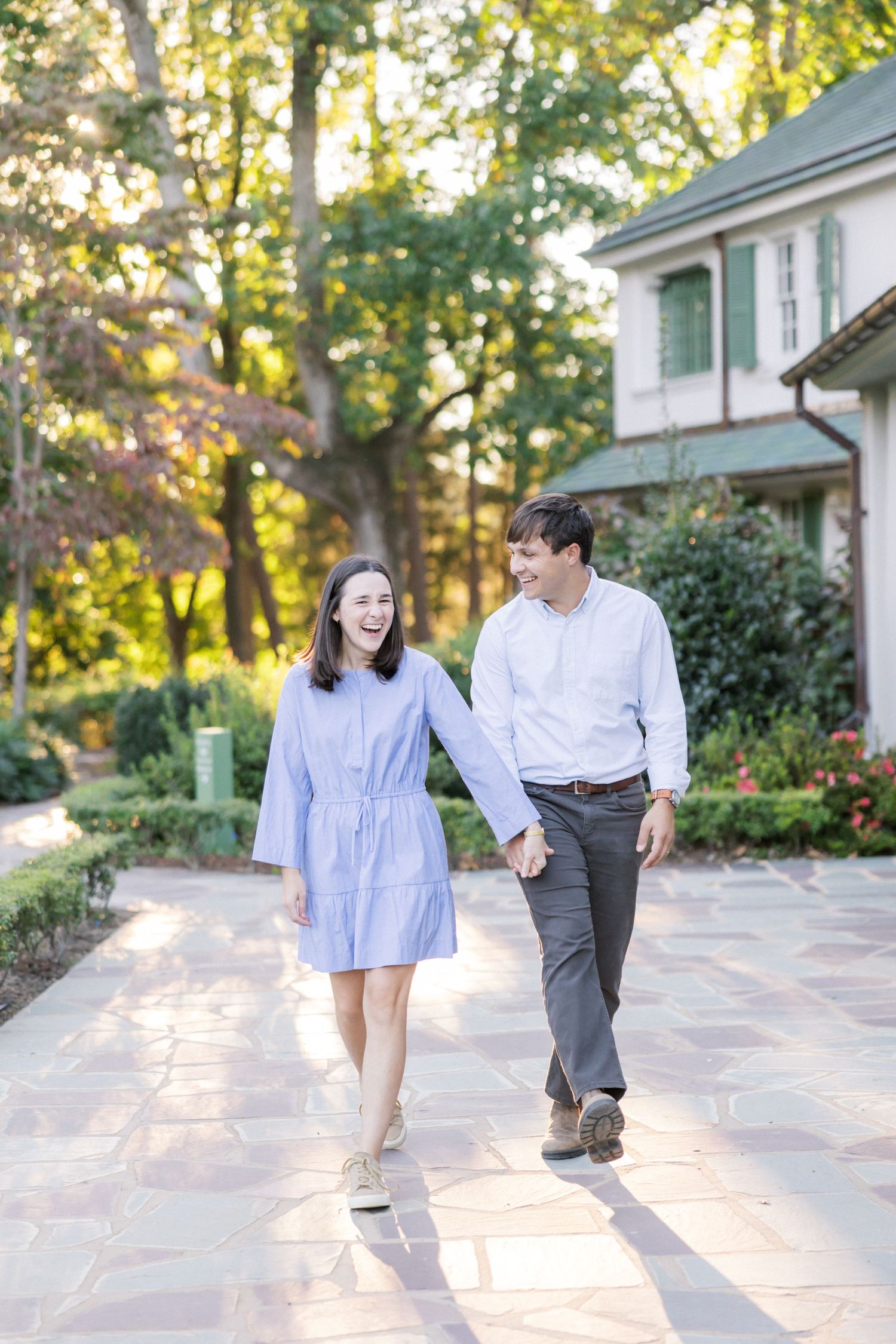A couple walks hand in hand along a stone path with warm evening sunlight casting long shadows.