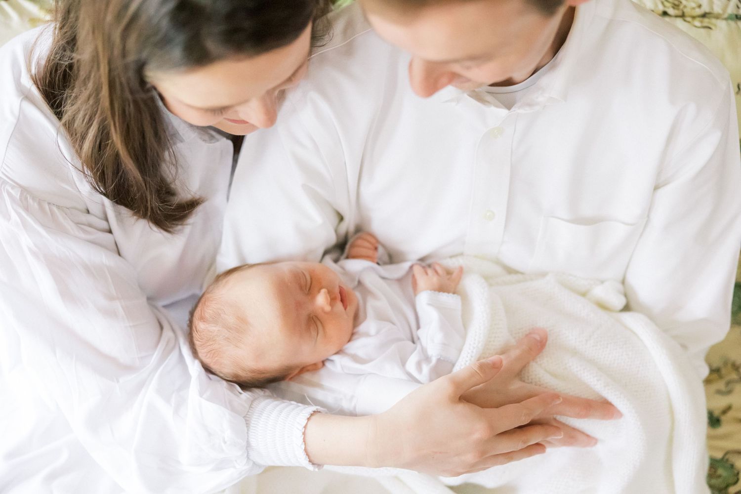Close-up view of parents in white clothing tenderly cradling their sleeping newborn baby.