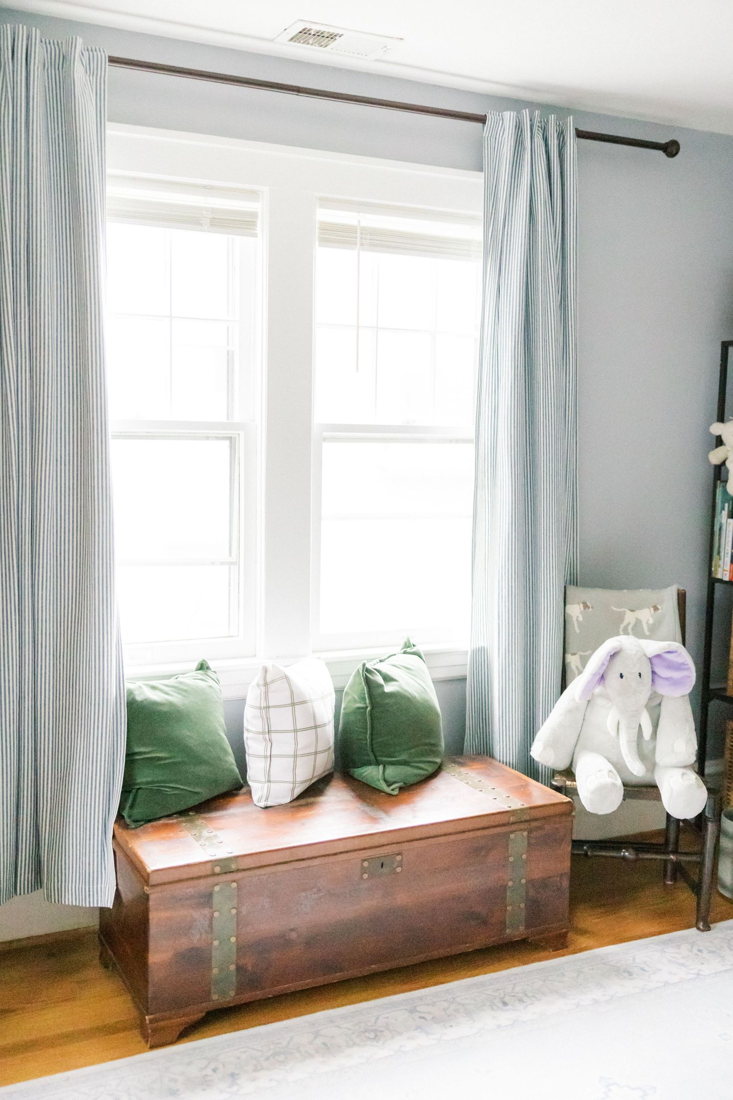 Cozy window seat with green pillows and vintage trunk in a nursery setting.