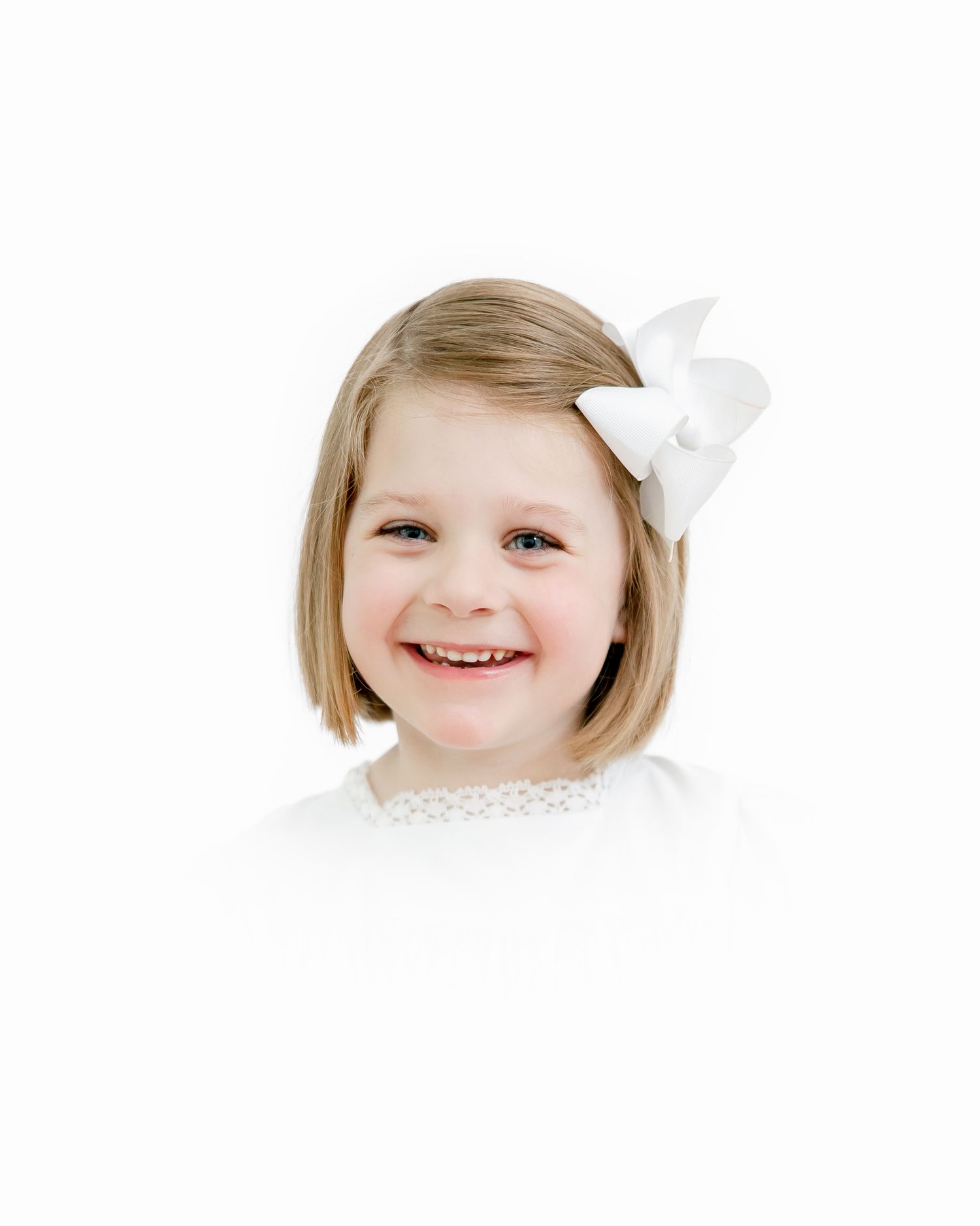 A young child with short blonde hair wearing white clothing and a bow hair accessory.