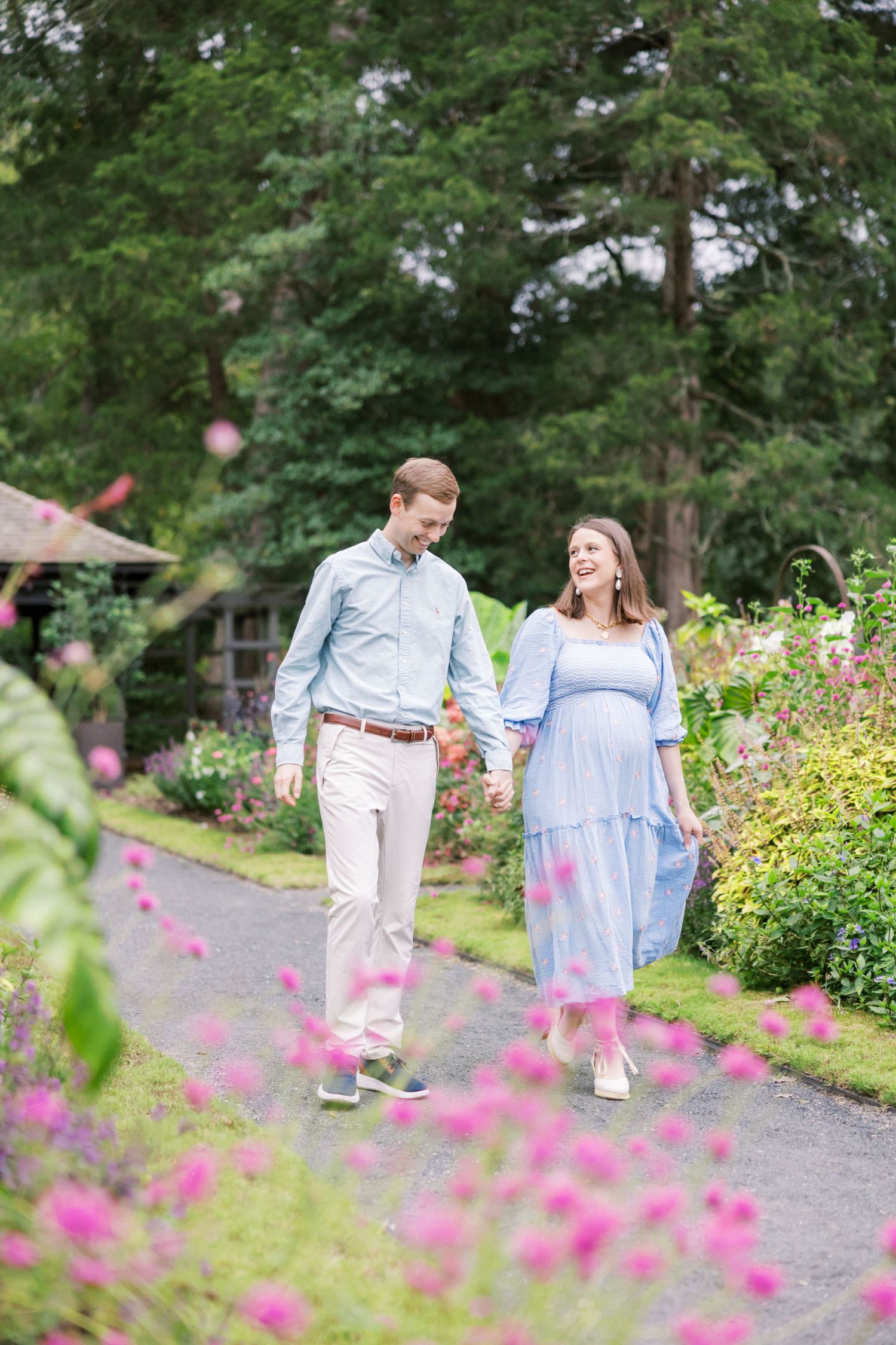 Couple walks hand in hand through flower garden with pink blooms.