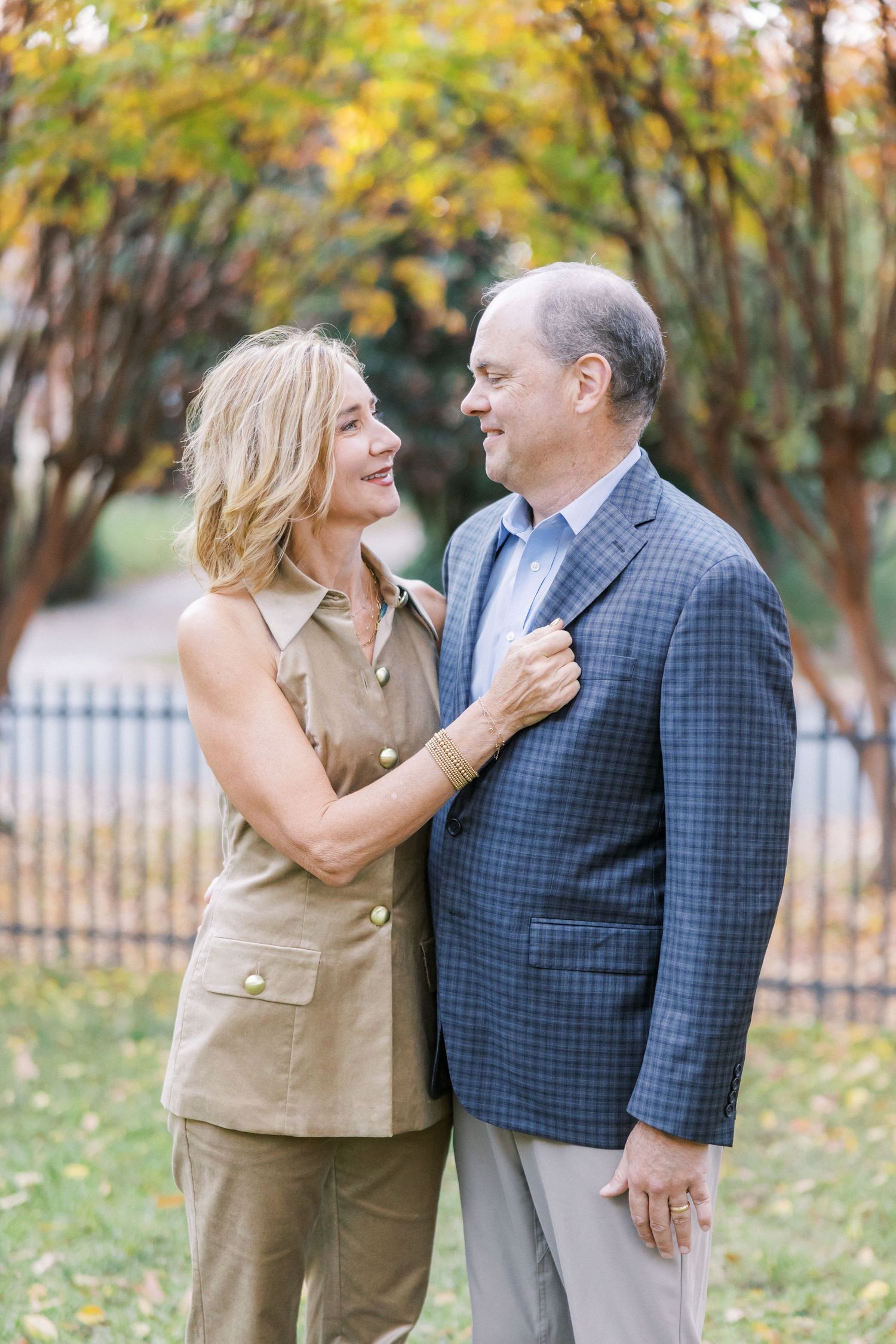 A couple shares an intimate moment outdoors during fall with trees displaying yellow foliage in background.