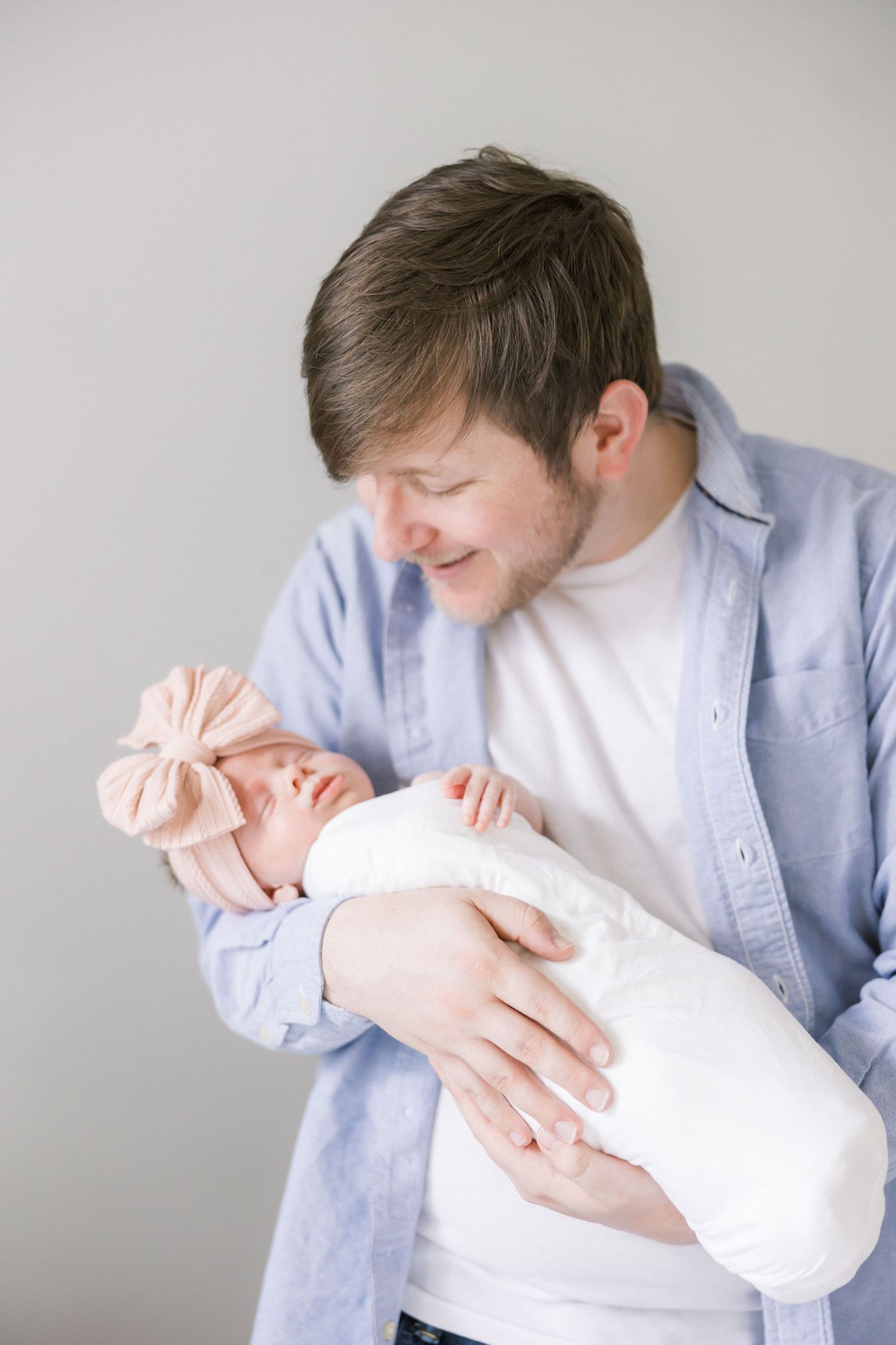 Caring adult in blue shirt tenderly holds swaddled newborn during portrait session.