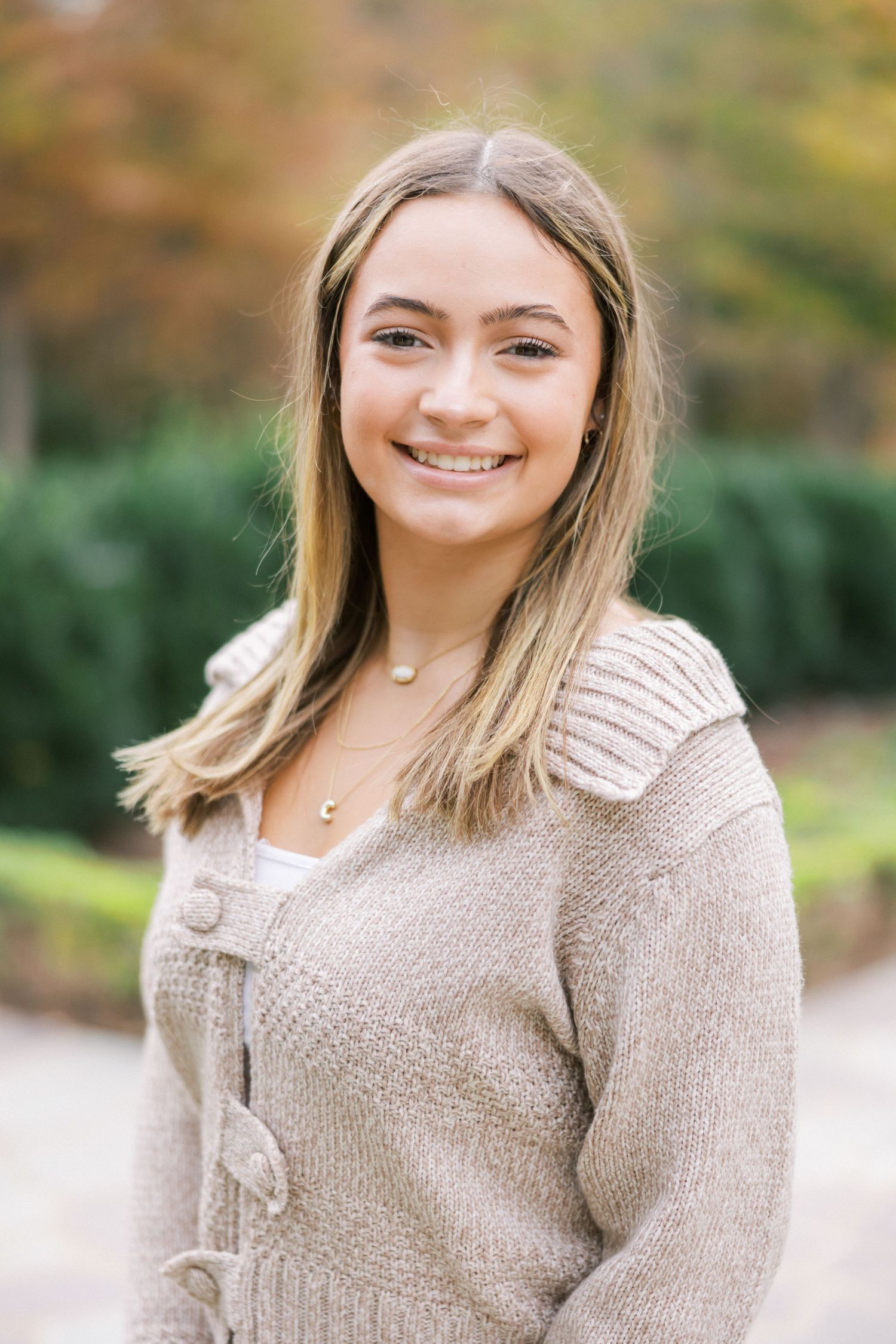 A portrait of someone wearing a beige knit sweater standing outdoors during autumn.