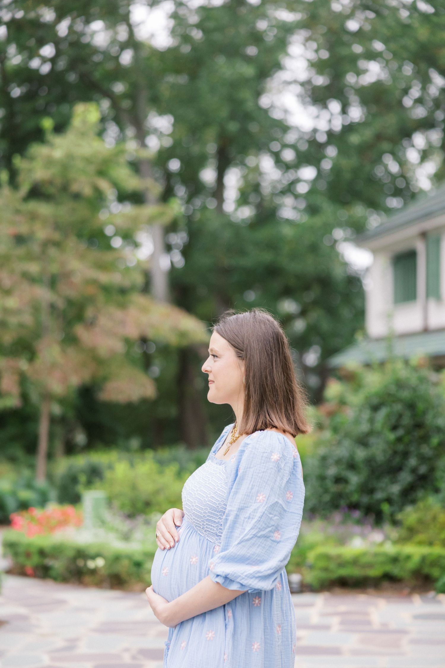 Side view of pregnant woman in flowing blue dress standing in garden.