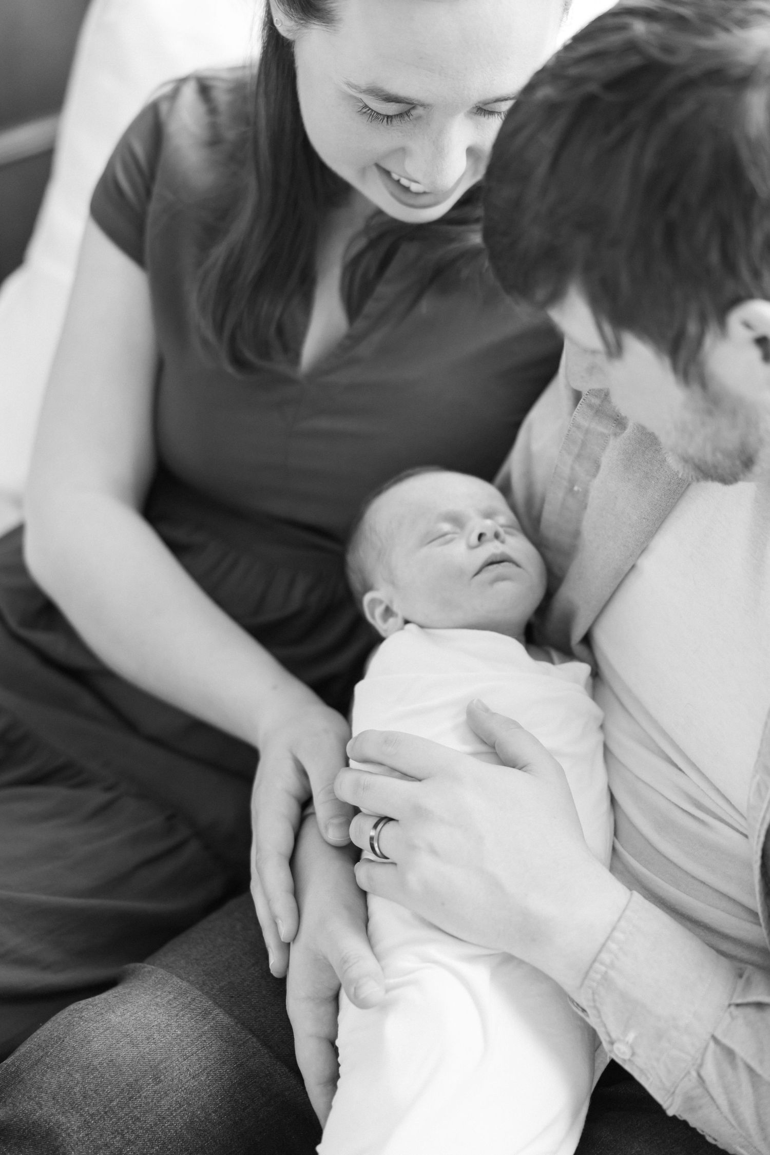 Parents in casual clothes share intimate moment with sleeping newborn.