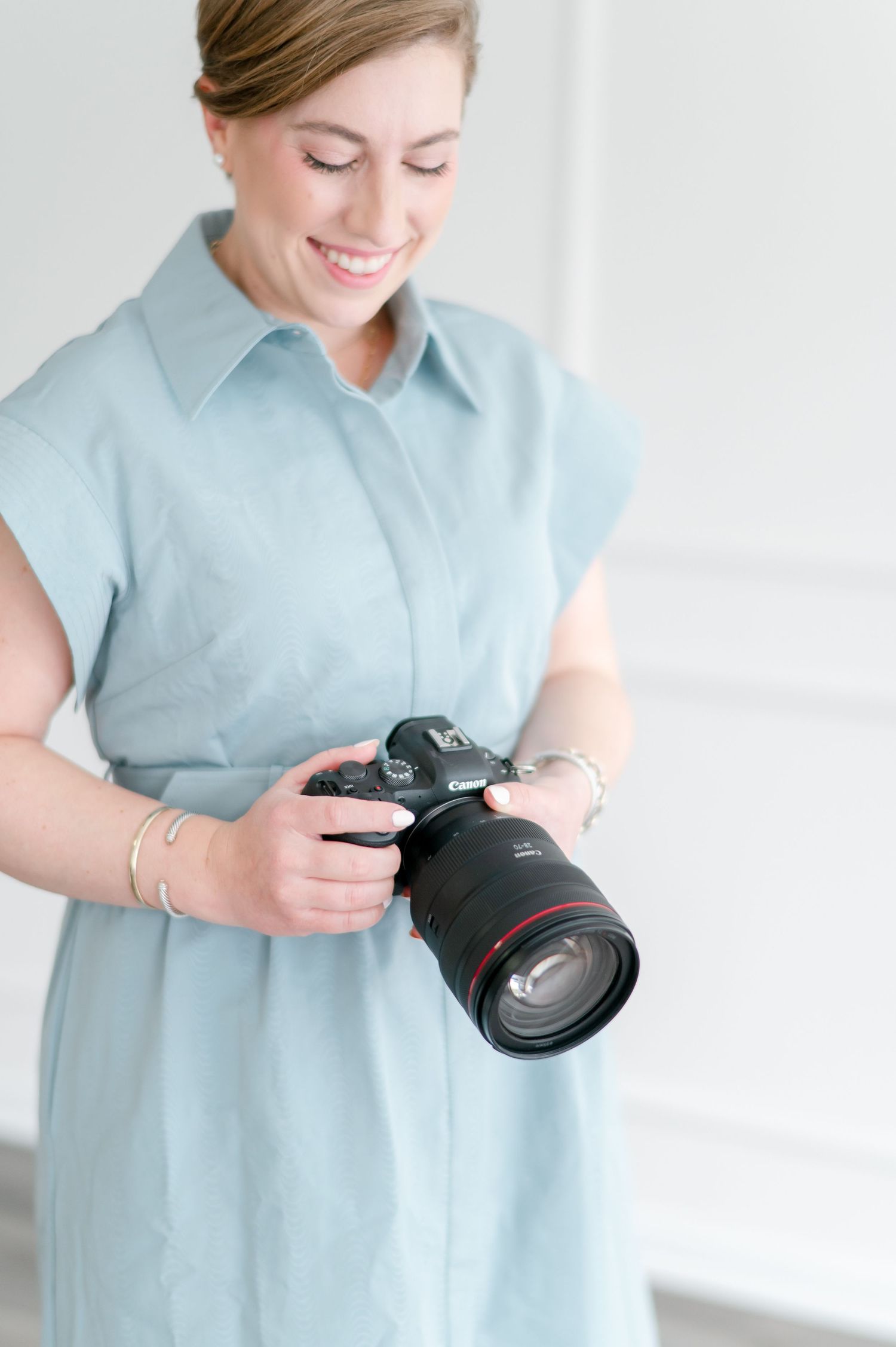Photographer examining professional camera while wearing light blue dress.