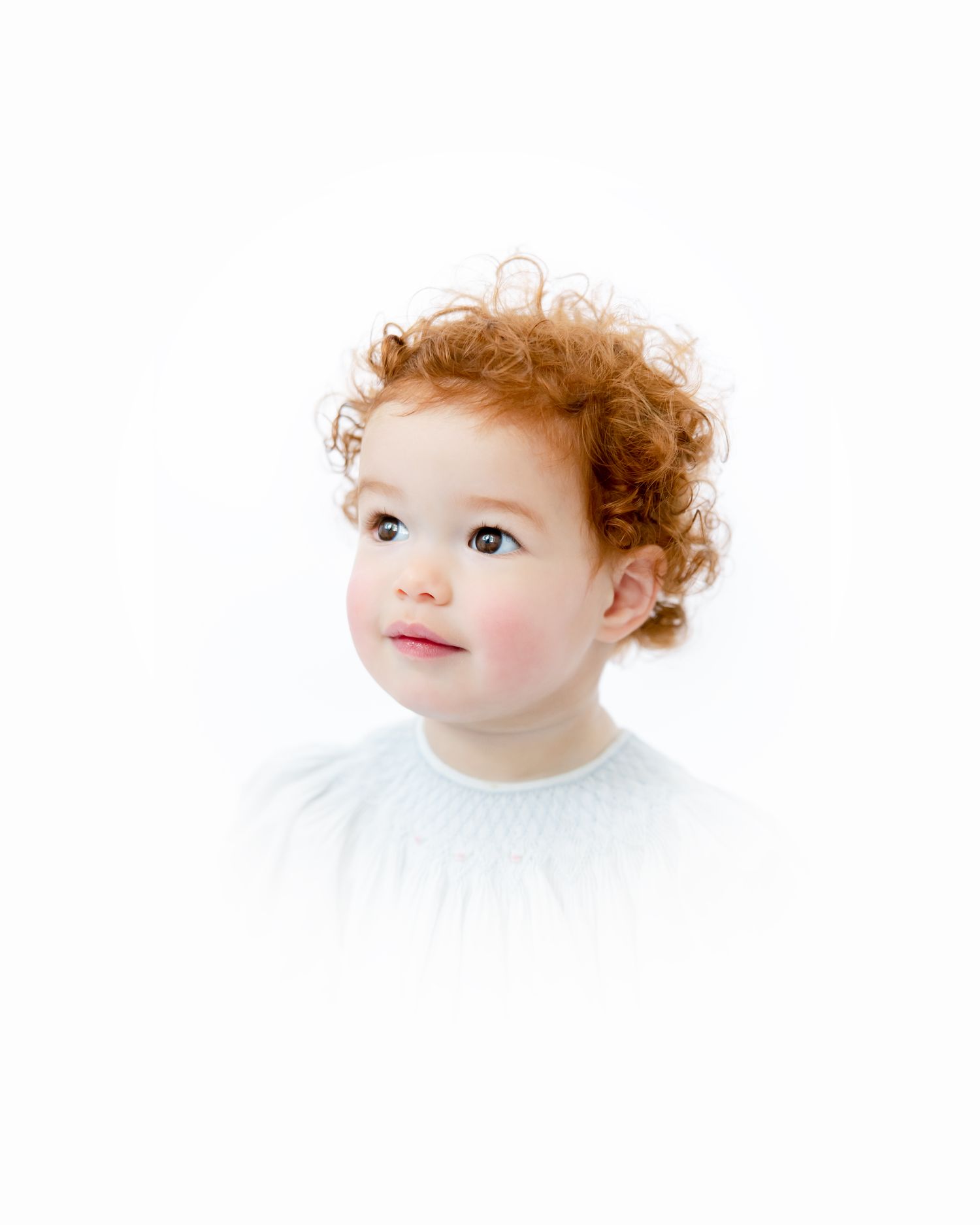 Portrait of a young child with curly red hair and a white shirt looking upwards dreamily.