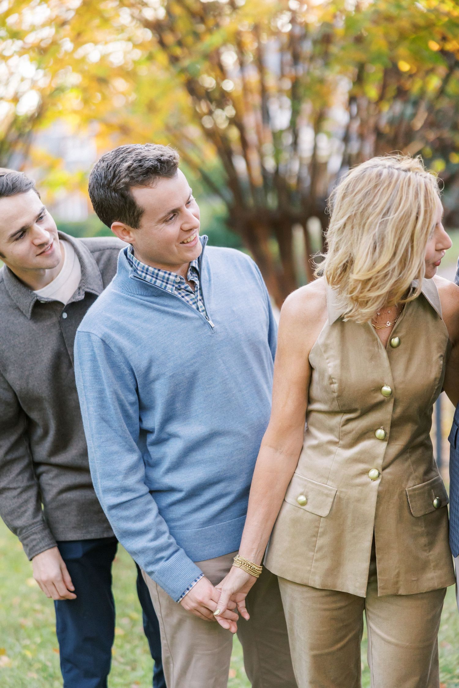 Three people enjoying a casual autumn walk together in a park with golden fall foliage in the background.
