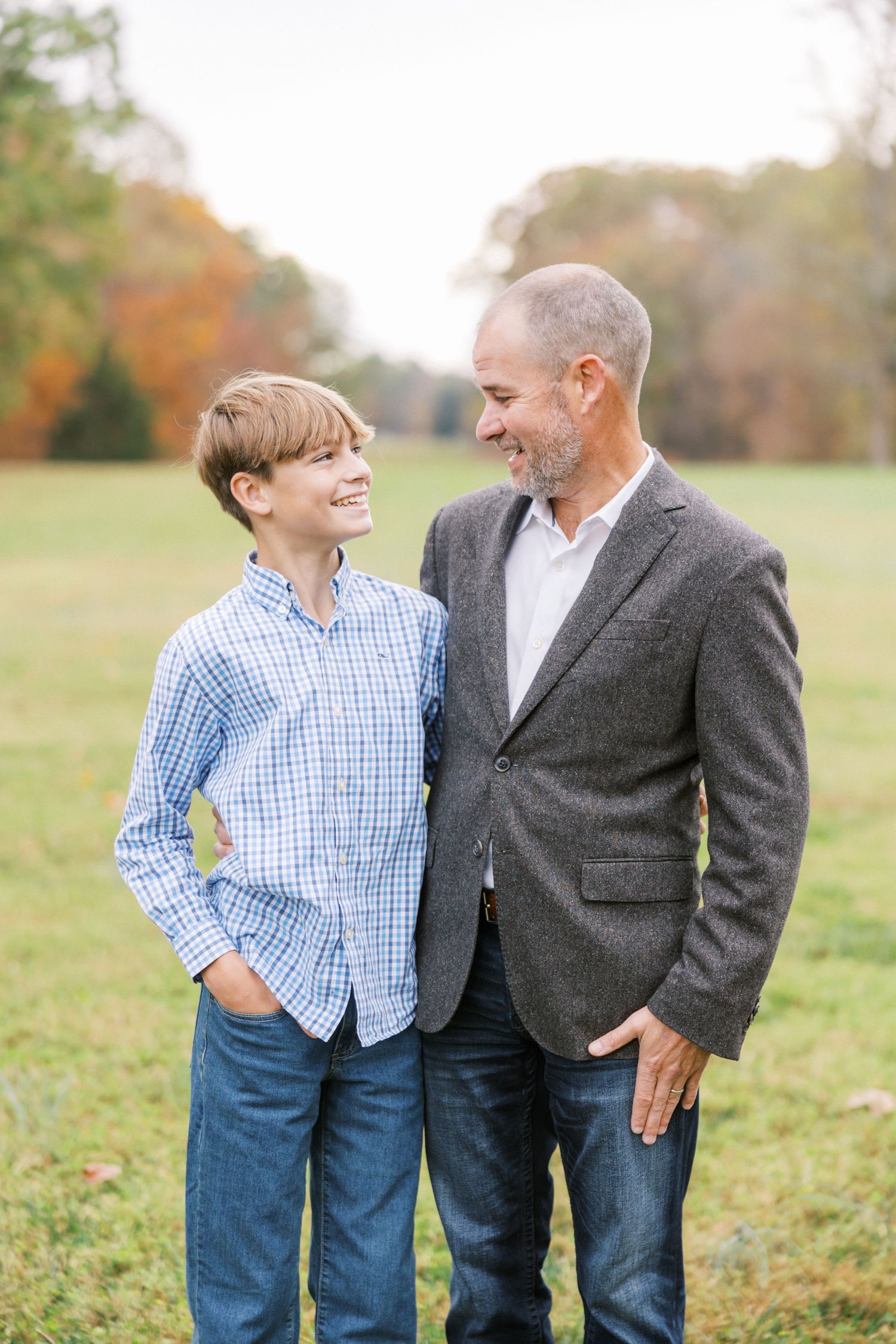 Two people share a candid moment together outdoors in a grassy field during fall.