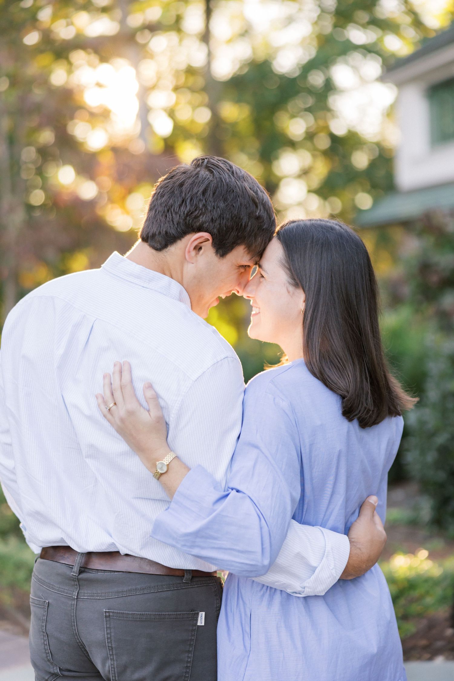 A tender moment between a couple in matching blue and white outfits against a sunlit garden backdrop.