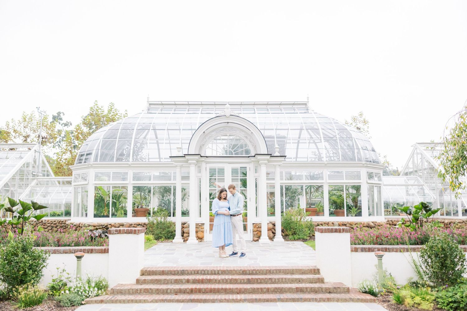 An elegant conservatory with white pillars and glass dome architecture in a garden setting.