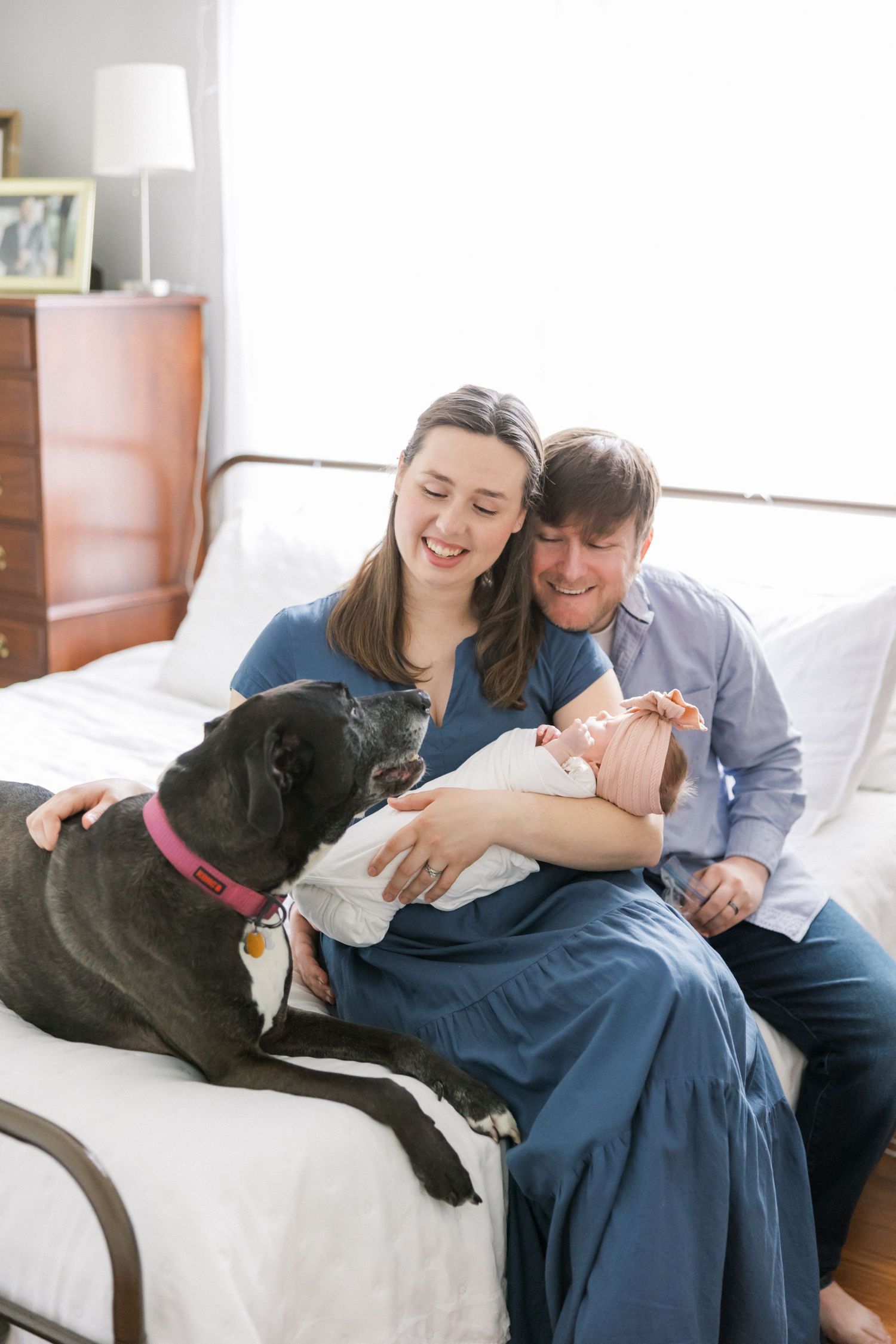 Happy family moment with dog and newborn baby on bed.
