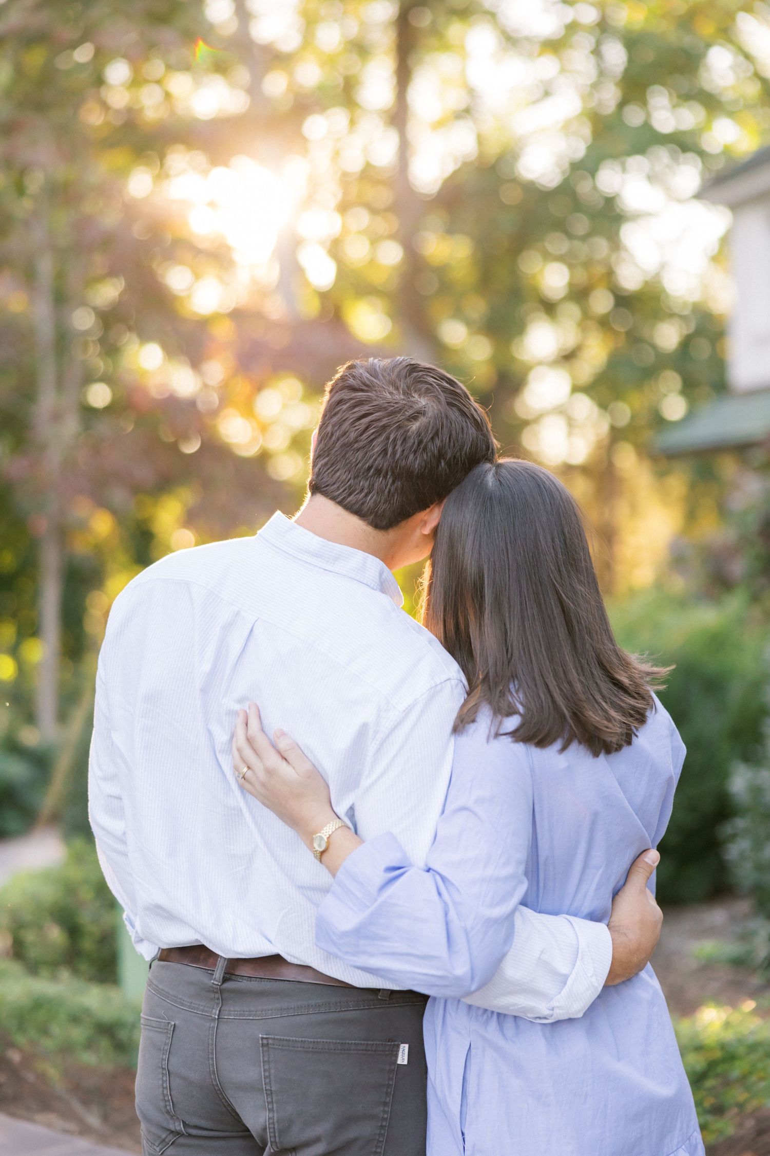 A couple in coordinating blue and white outfits embrace while facing away from the camera in a garden setting.