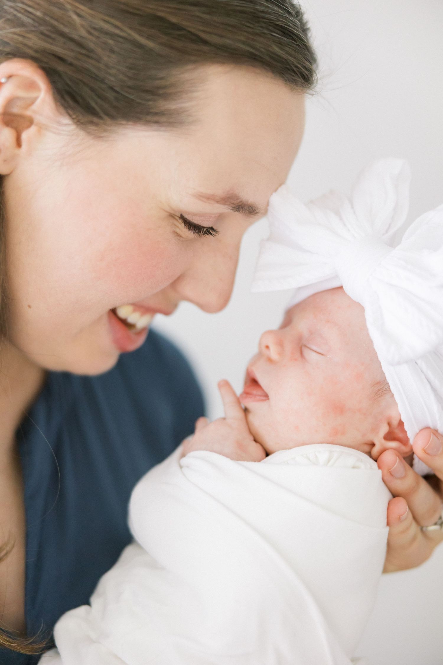 Intimate portrait of parent and newborn sharing gentle moment against light background.