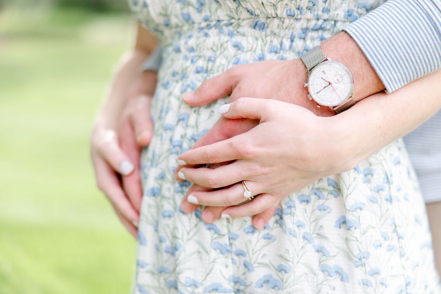 Close-up detail of hands resting on a floral dress with a watch visible in the soft natural lighting.