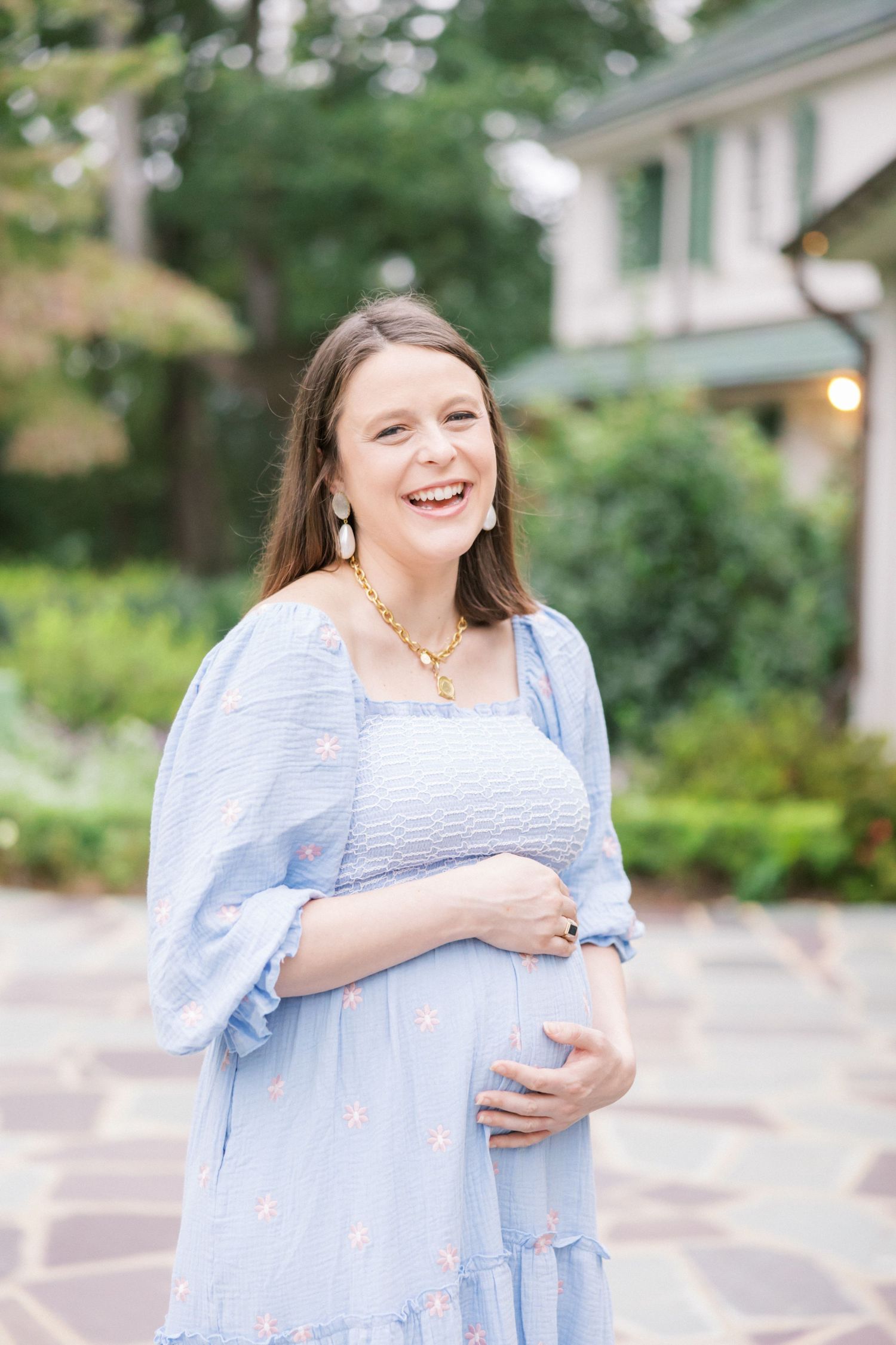 Woman in light blue dress smiles joyfully while standing in garden setting.