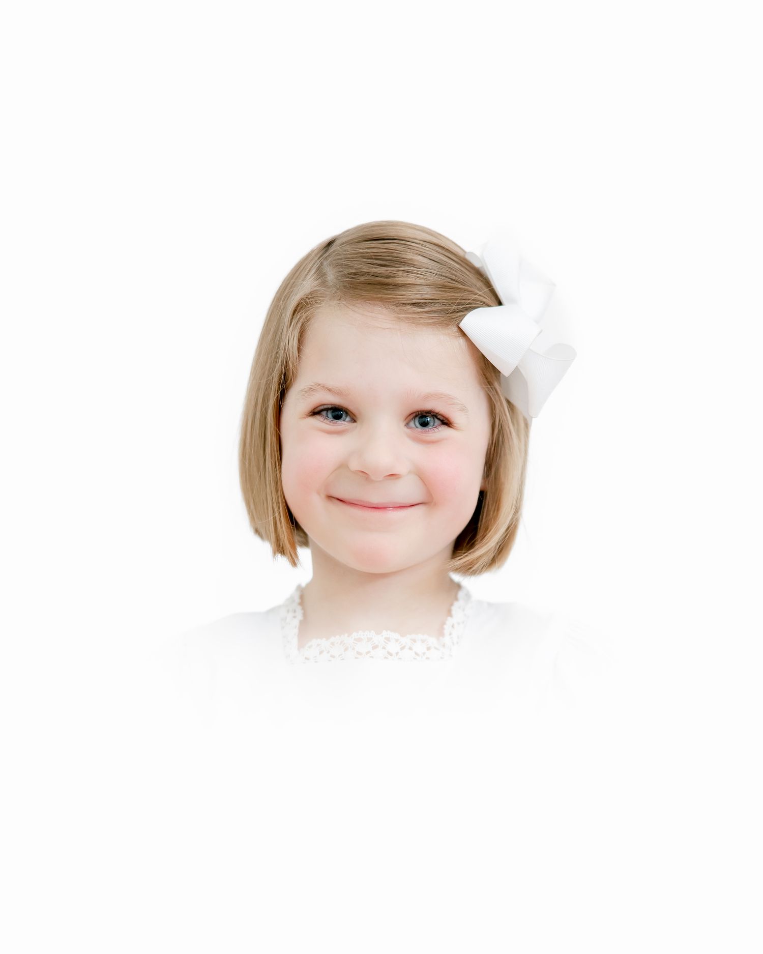 Portrait of a young child with blonde bob-length hair and a white hair bow on a white background.