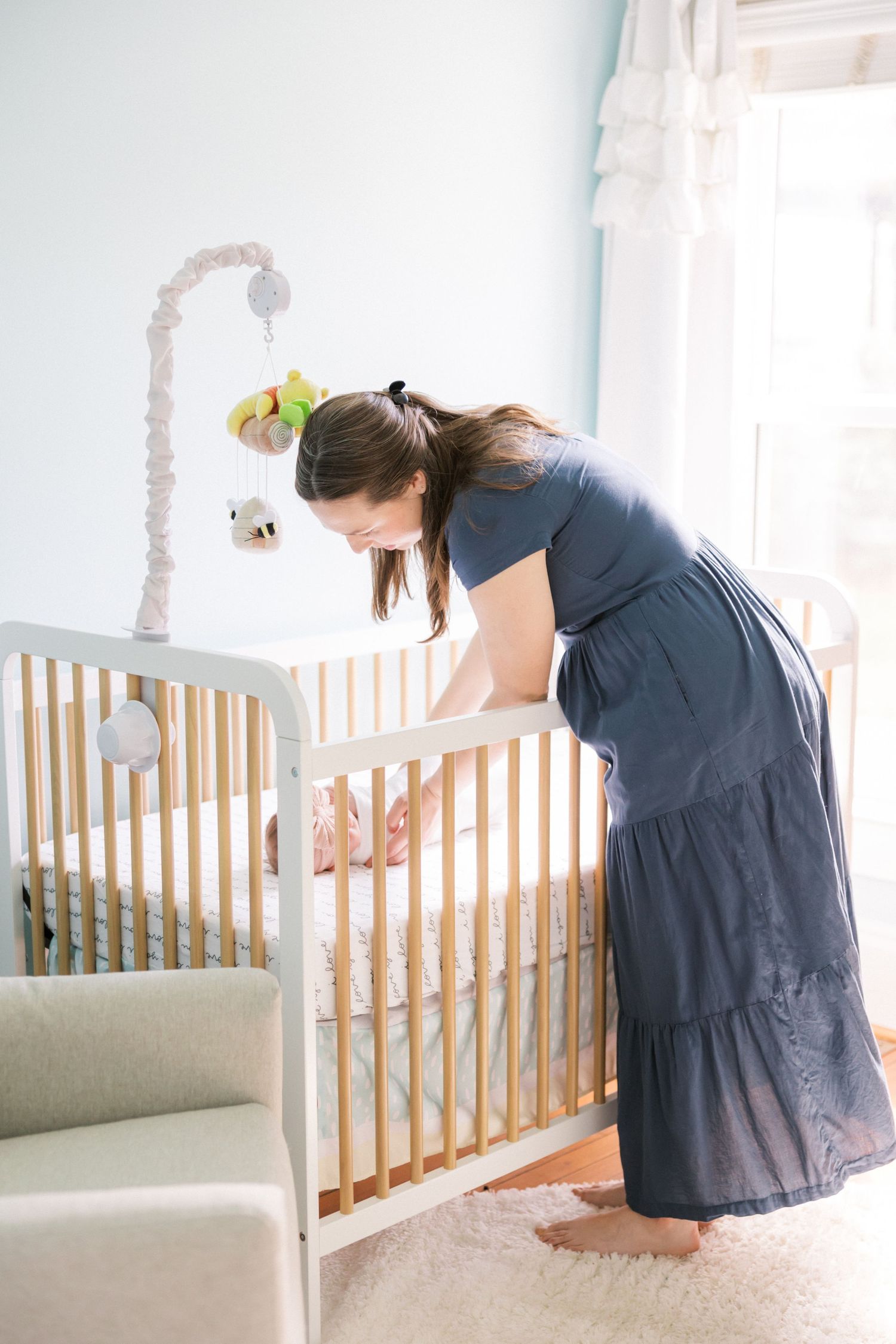 A woman in a blue dress arranging items in a wooden baby crib.