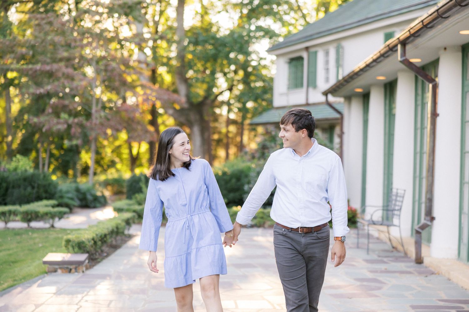 A couple takes a romantic stroll together along a garden path beside a white house.