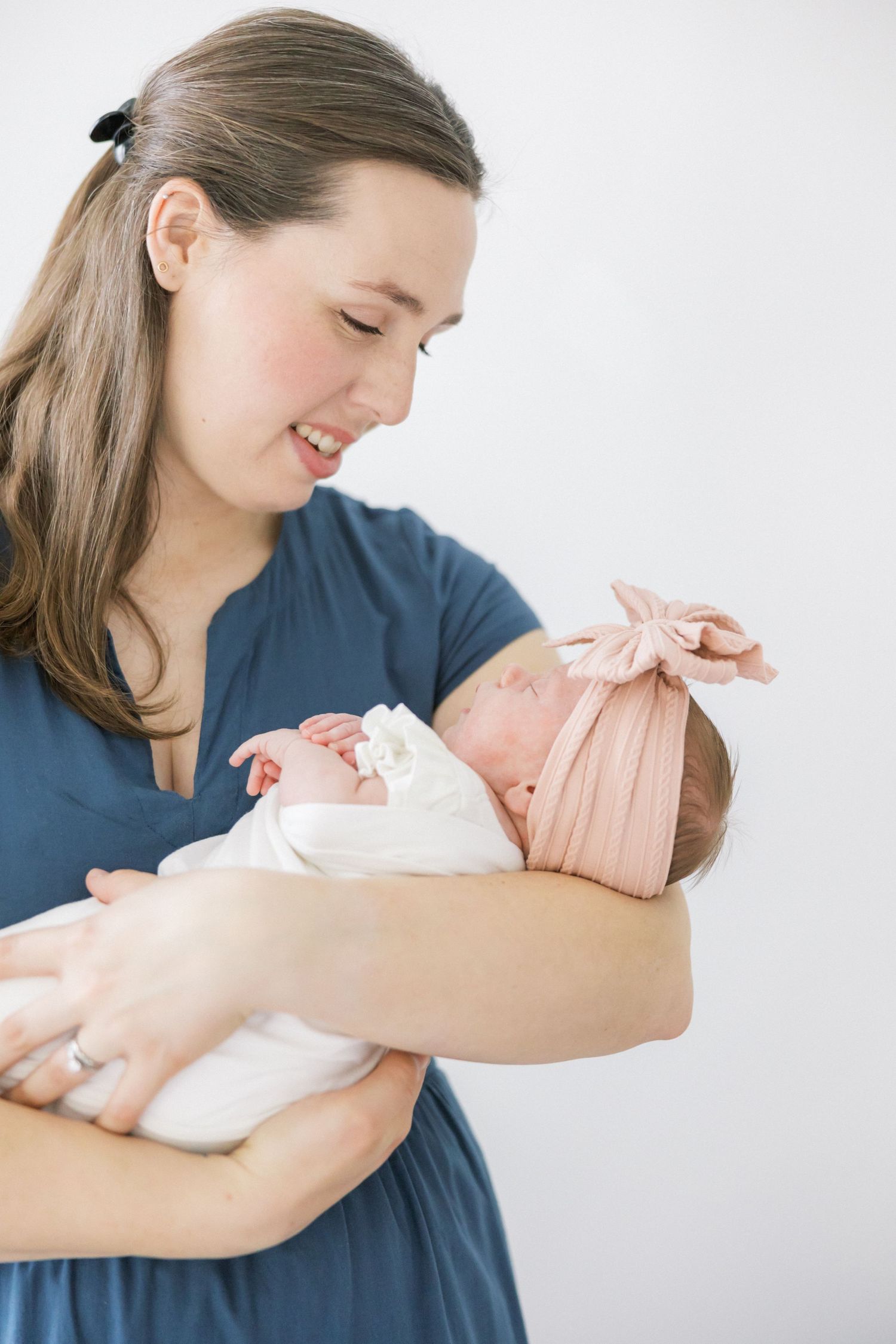 Joyful caregiver cradles sleeping infant wearing pink bow during professional photoshoot.
