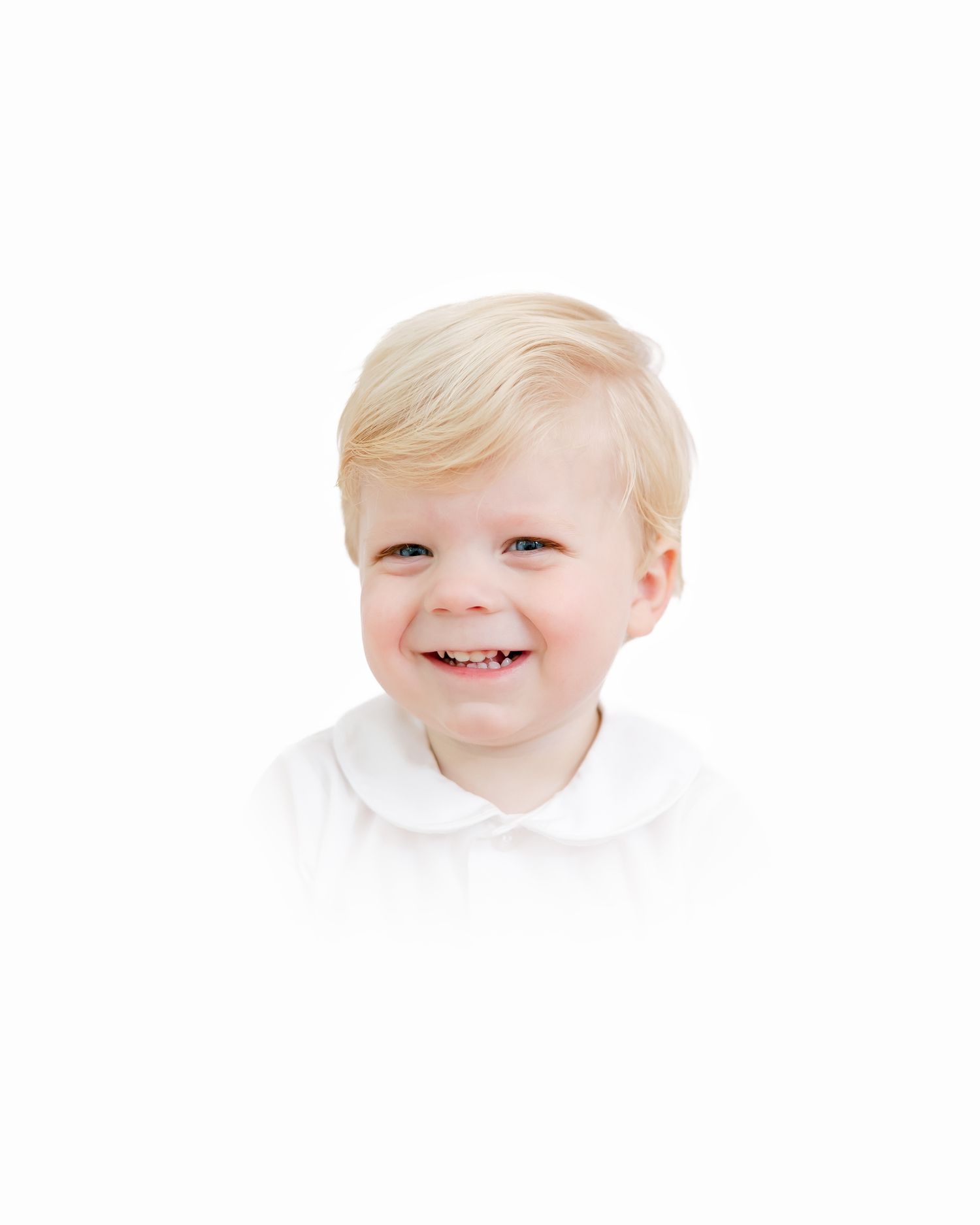 Smiling toddler wearing a white collared shirt against a bright white background.