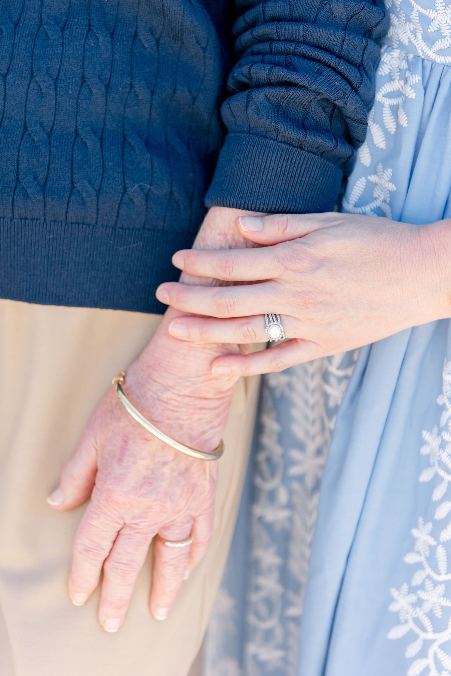 A gentle moment captured between two hands wearing rings and bracelets against blue clothing and cream fabric.