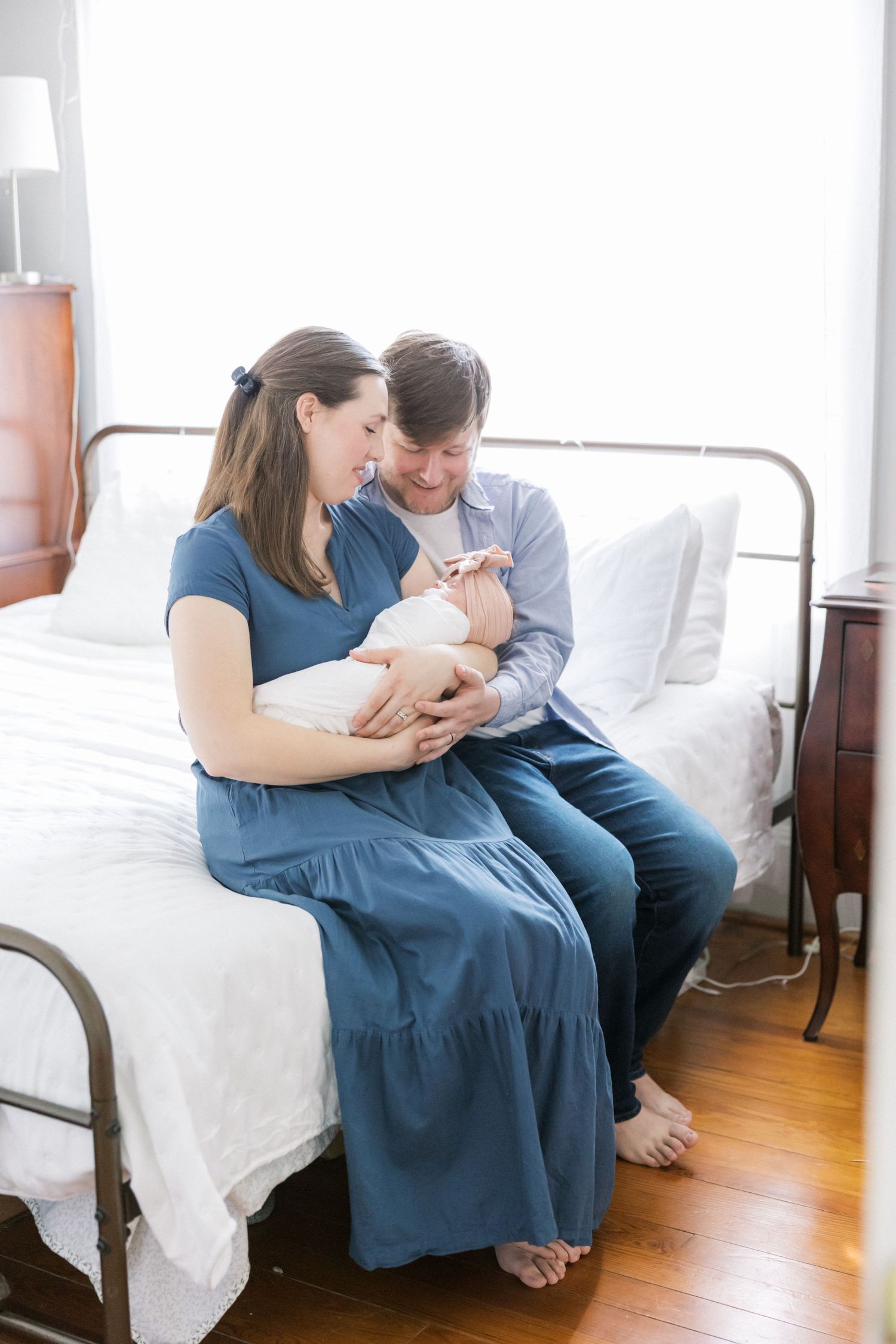 Couple sitting on bed cradling their newborn baby while wearing coordinating blue outfits.